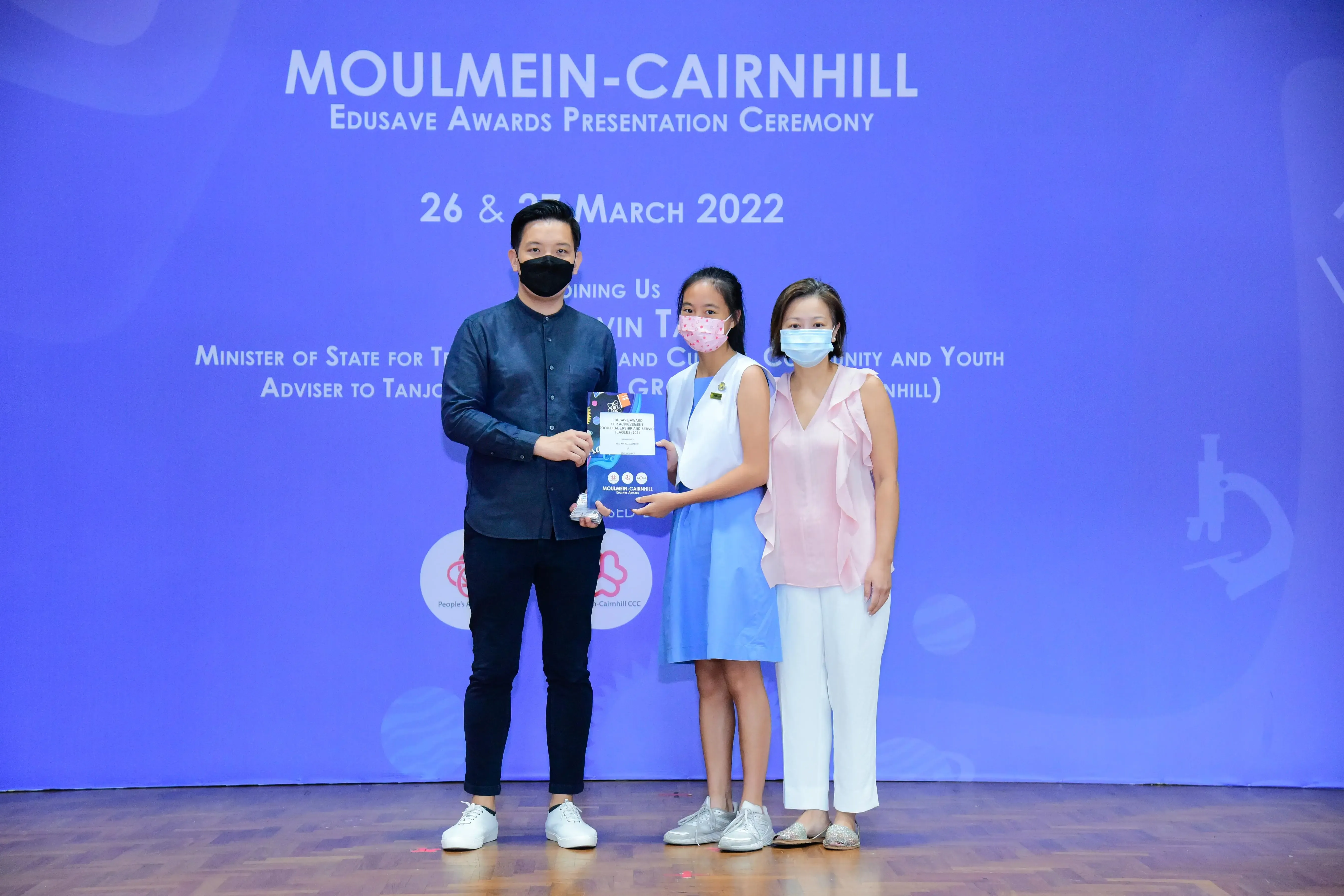 Three masked people pose holding an award at the Moulmein-Cairnhill Edusave Awards Ceremony, March 2022.