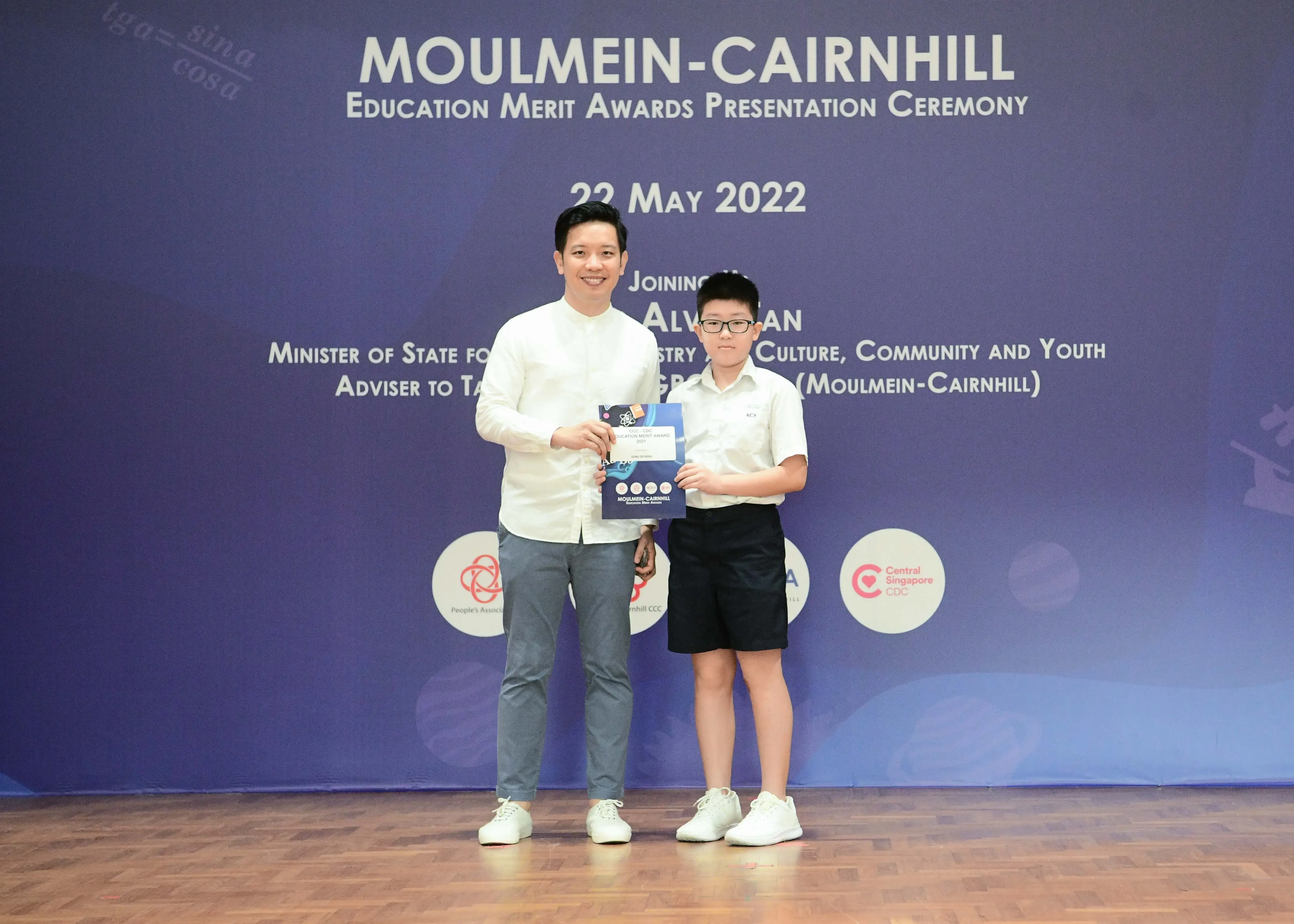 An adult and a young boy hold a certificate together at the Moulmein-Cairnhill Education Merit Awards on 22 May 2022.