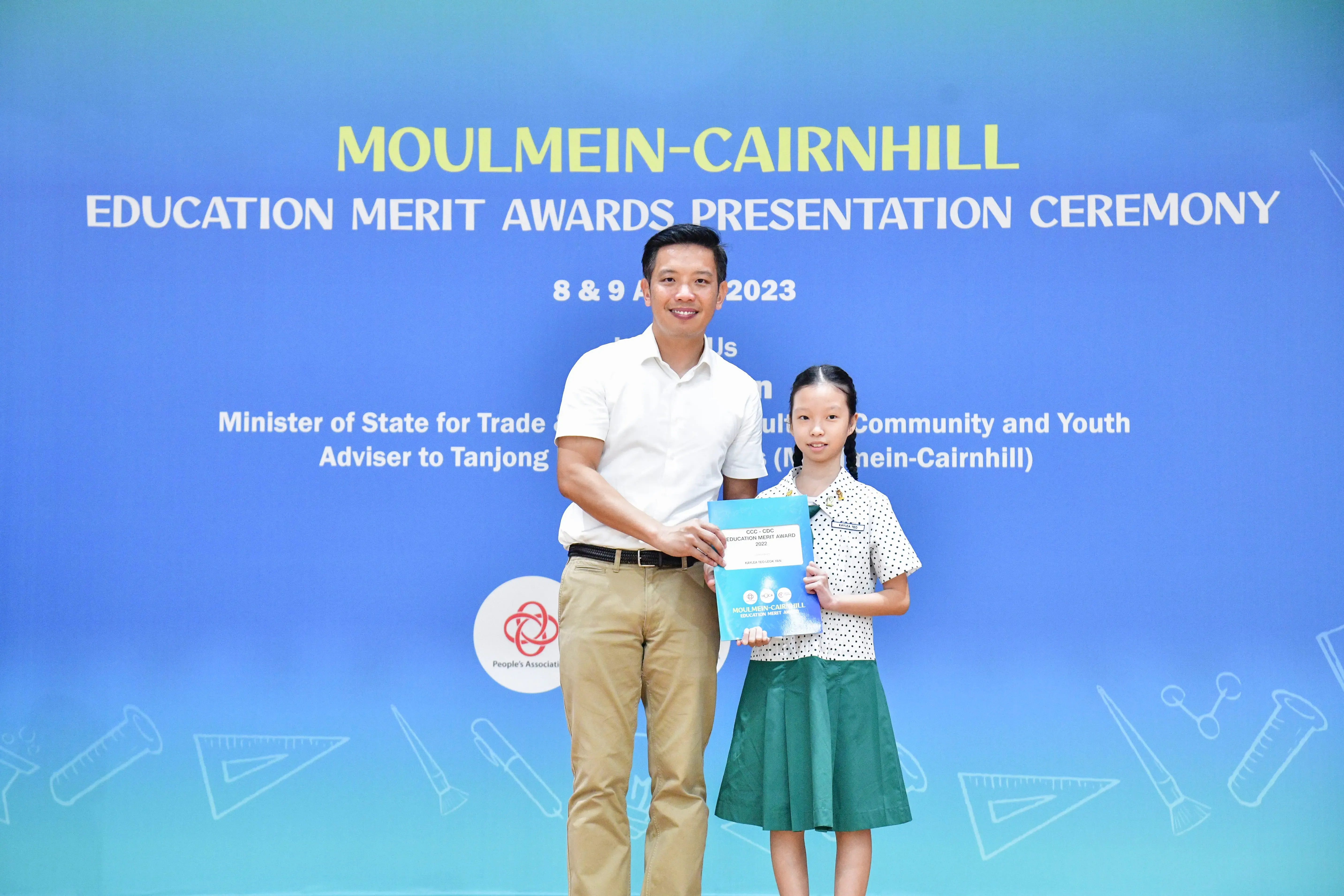 A man and a young girl hold an award certificate at the Moulmein-Cairnhill Education Merit Awards Ceremony 2023.