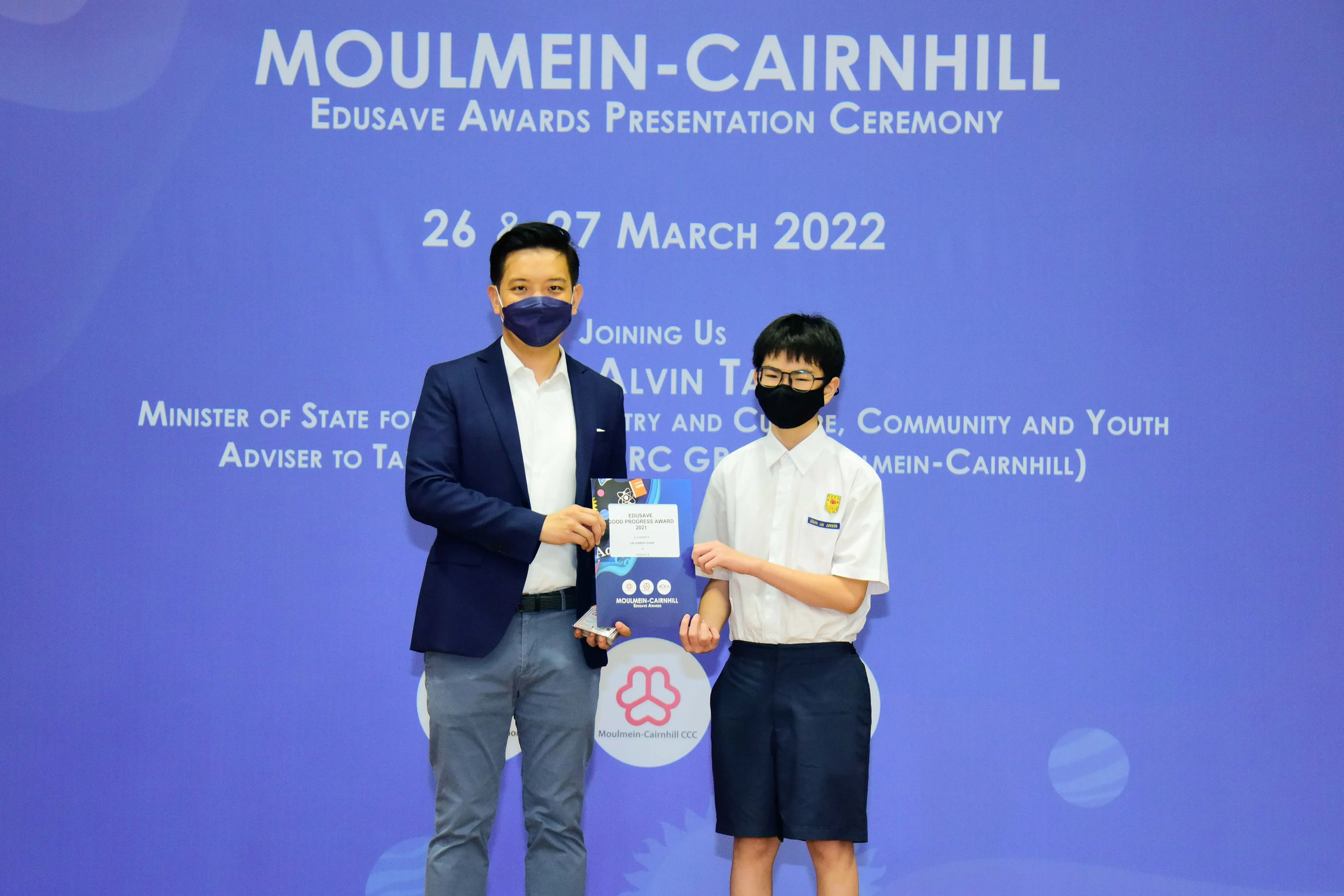 Two masked individuals hold an award at the Moulmein-Cairnhill Edusave Awards Presentation Ceremony, March 2022.