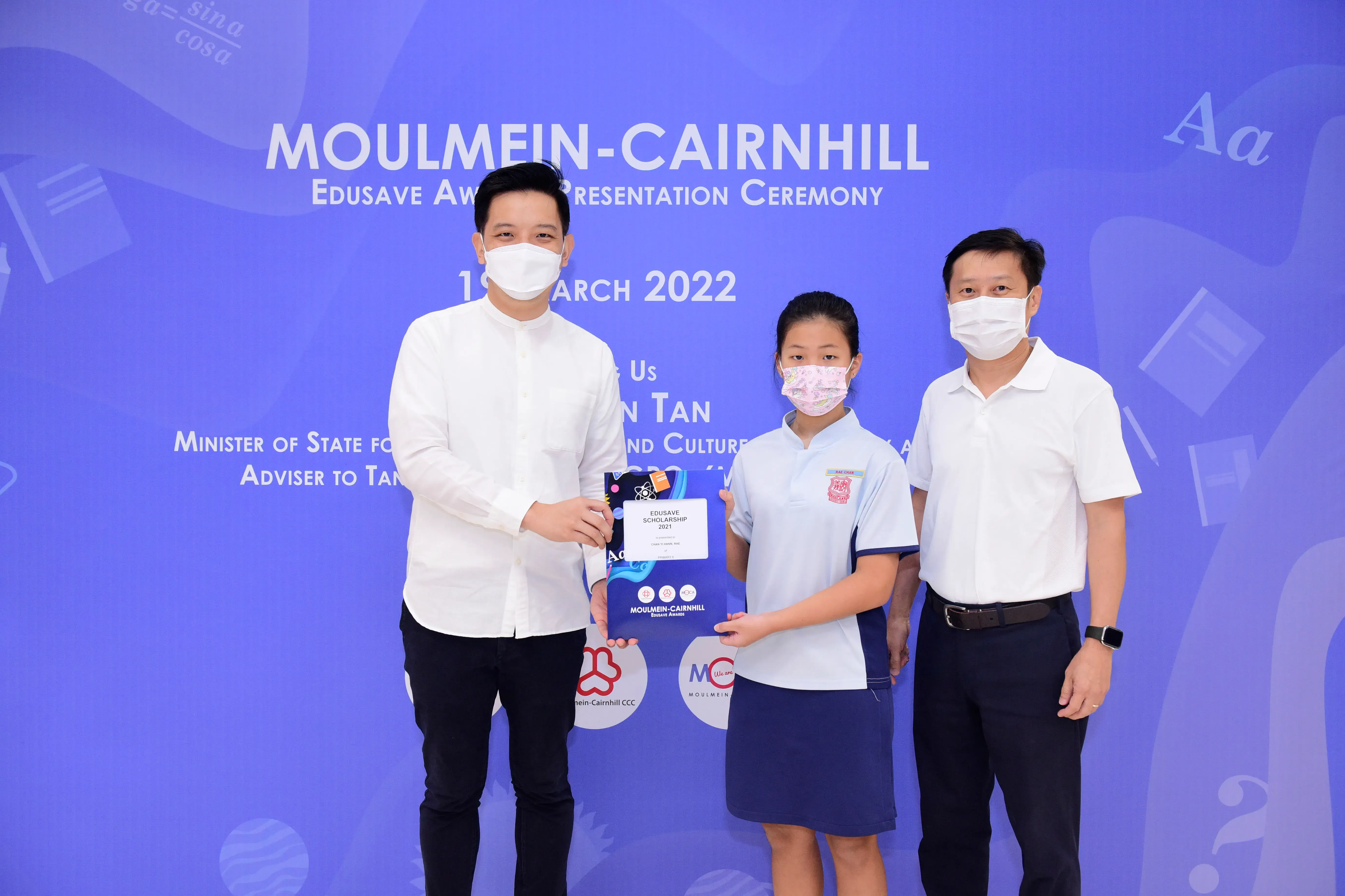 Two men and a student in school uniform hold an Edusave Scholarship award at the Moulmein-Cairnhill ceremony in 2022.