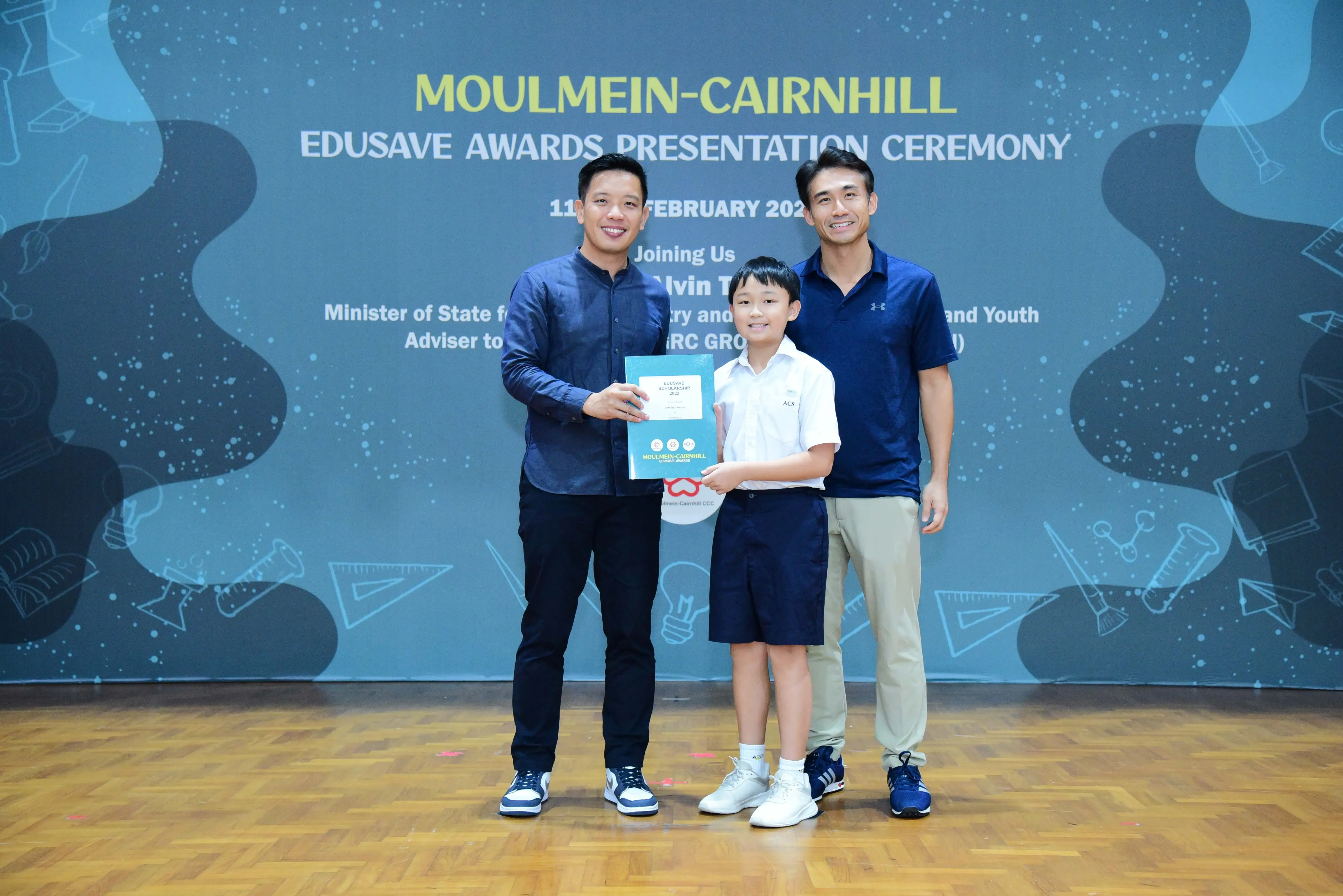 Two men and a young student in school uniform pose holding an award at the Moulmein-Cairnhill Edusave Awards Ceremony.