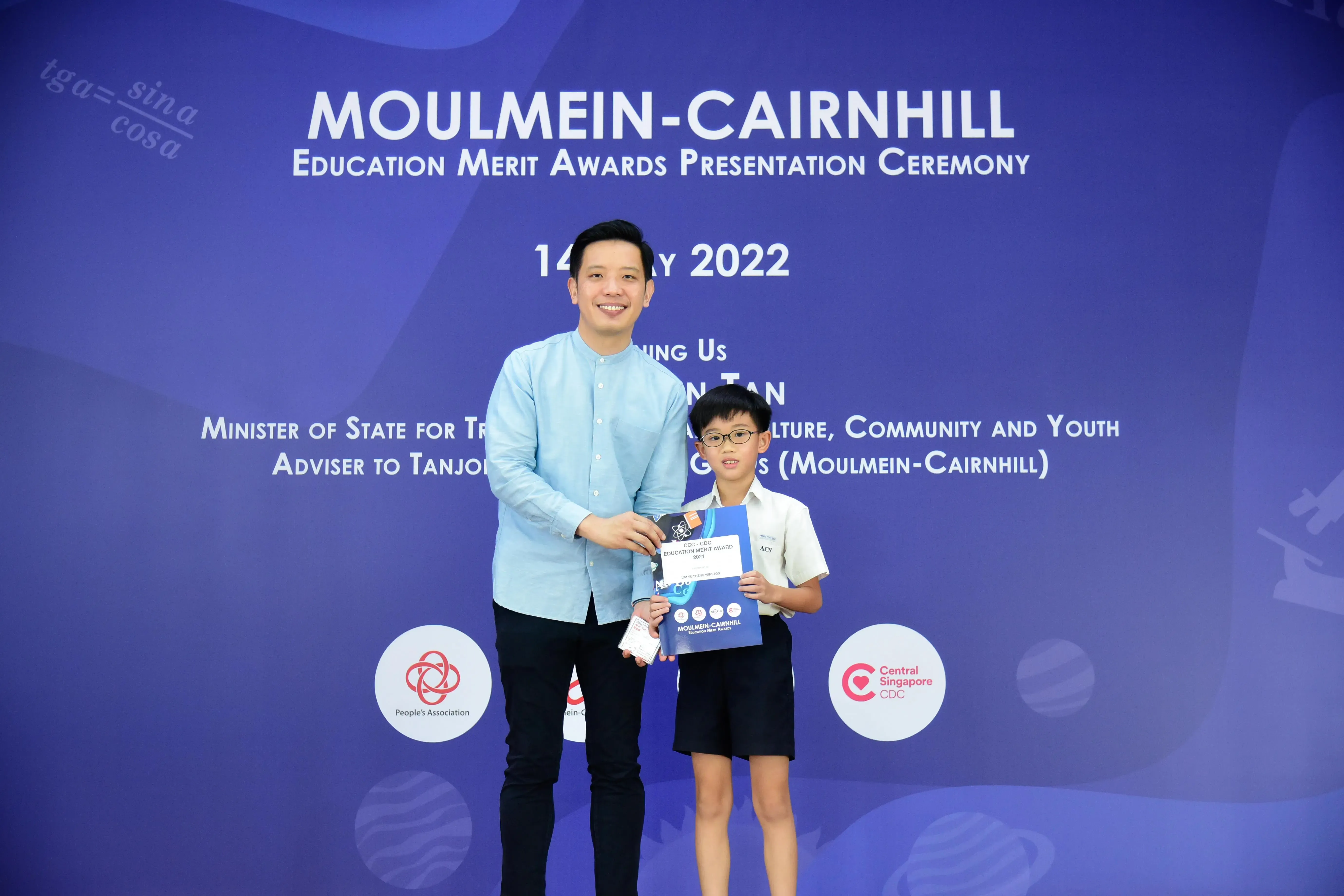 Adult and young boy holding an award certificate at the Moulmein-Cairnhill Education Merit Awards Ceremony 2022.