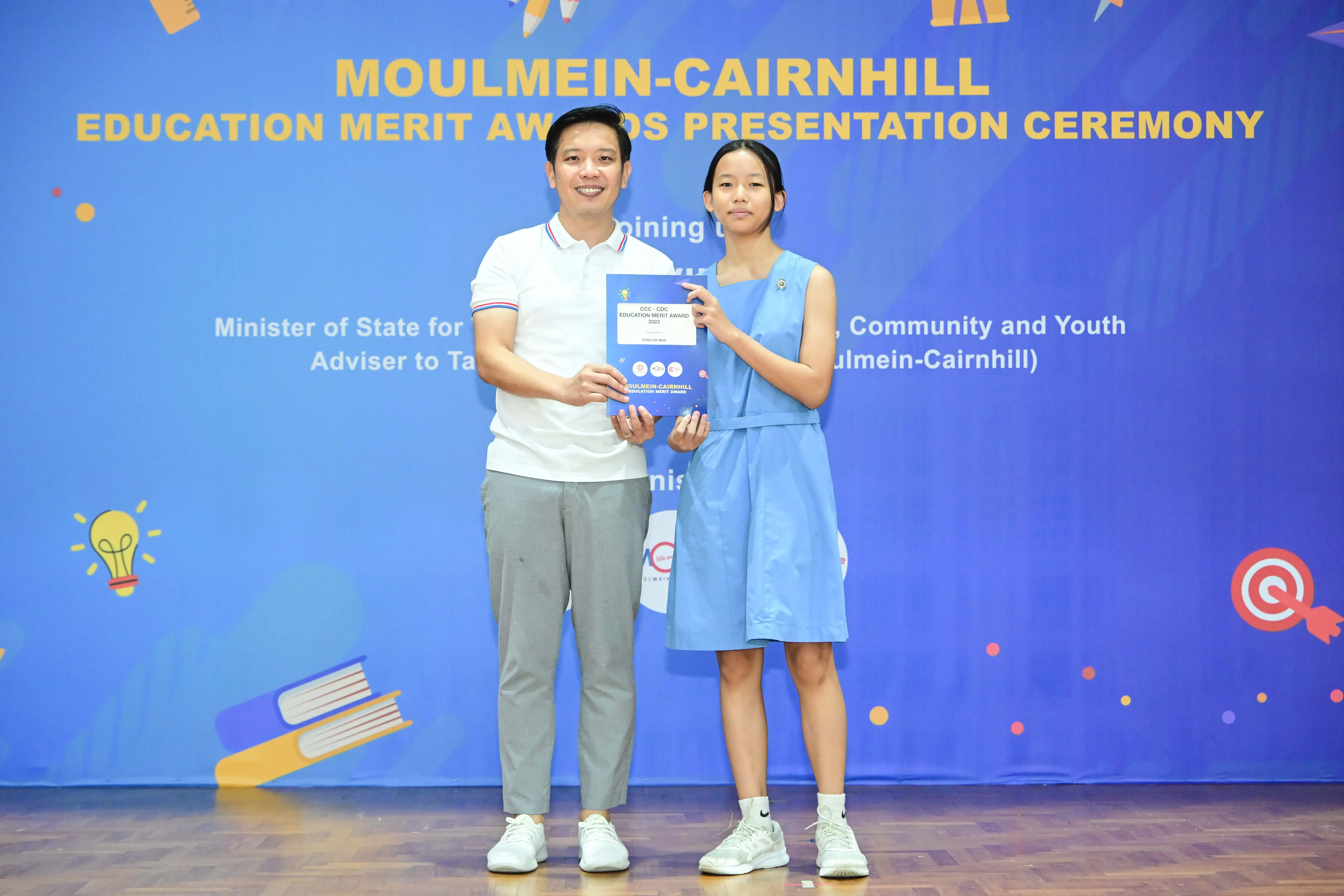 A man and a girl hold a blue award certificate at the Moulmein-Cairnhill Education Merit Awards Presentation Ceremony.