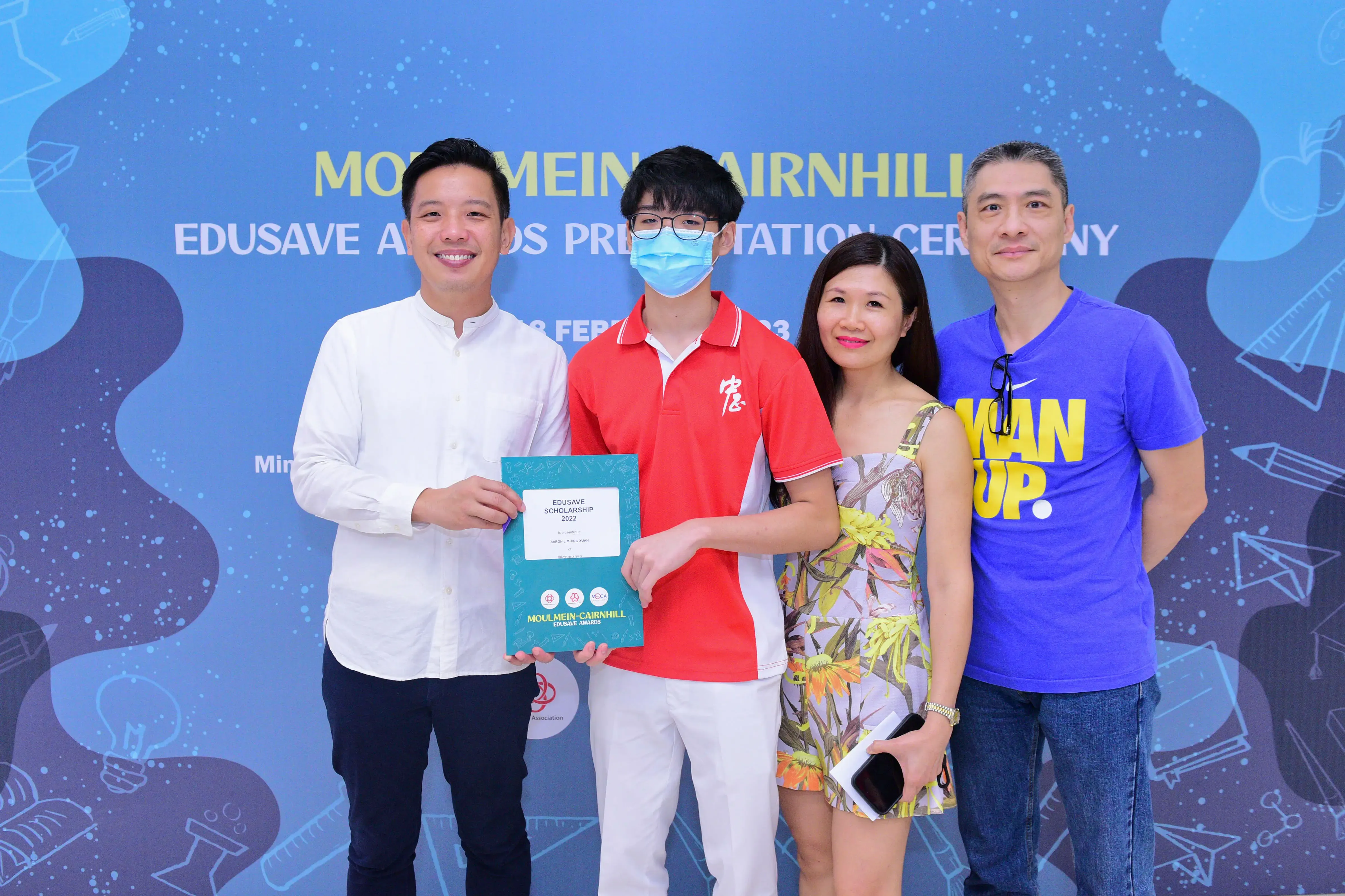 Four people pose at a Moulmein-Cairnhill Edusave Awards ceremony, holding a 2022 scholarship certificate.