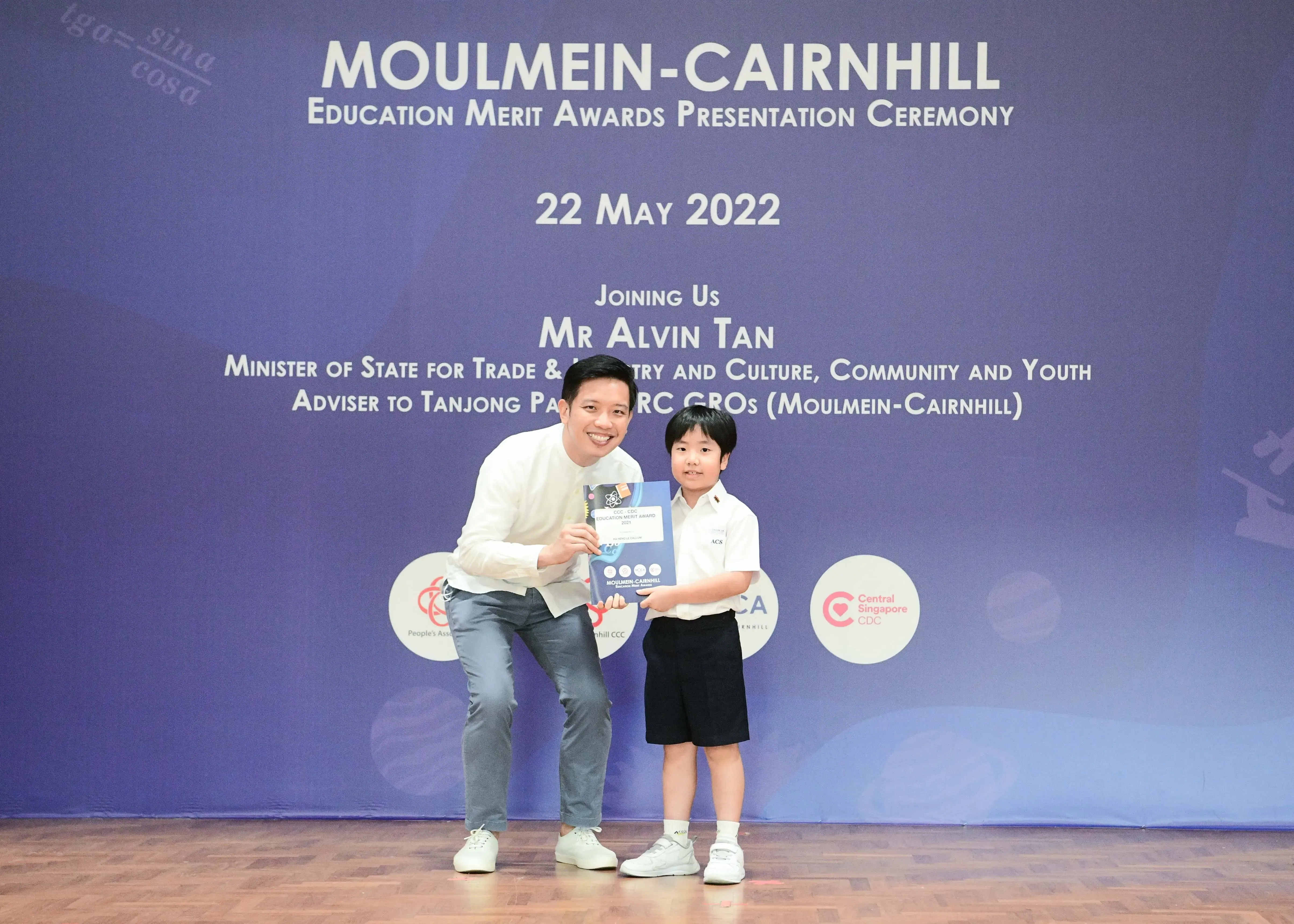 Adult and young student hold an award at the Moulmein-Cairnhill Education Merit Awards Ceremony on 22 May 2022.
