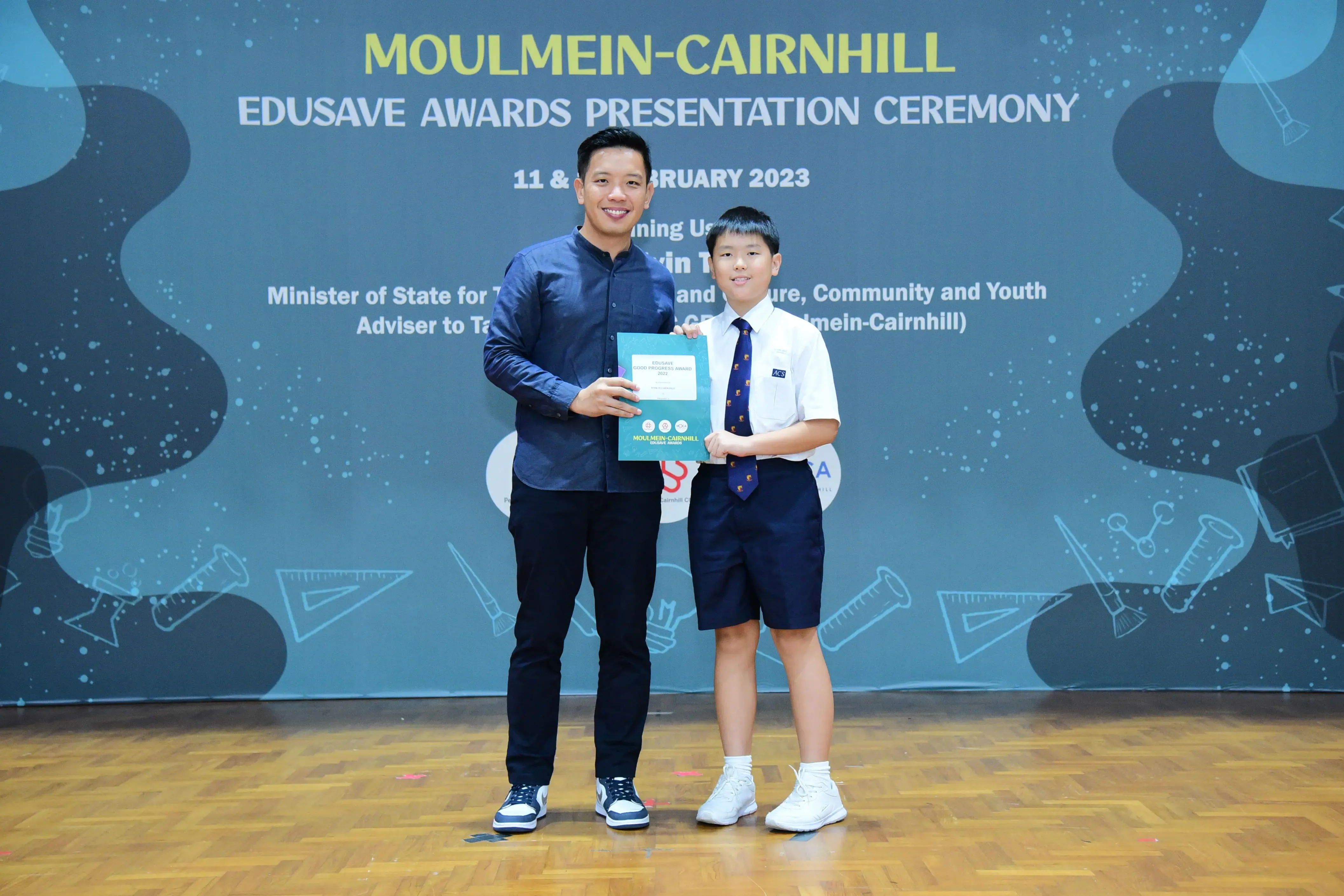 An adult and a uniformed schoolboy hold an award certificate at the Moulmein-Cairnhill Edusave Awards Ceremony 2023.