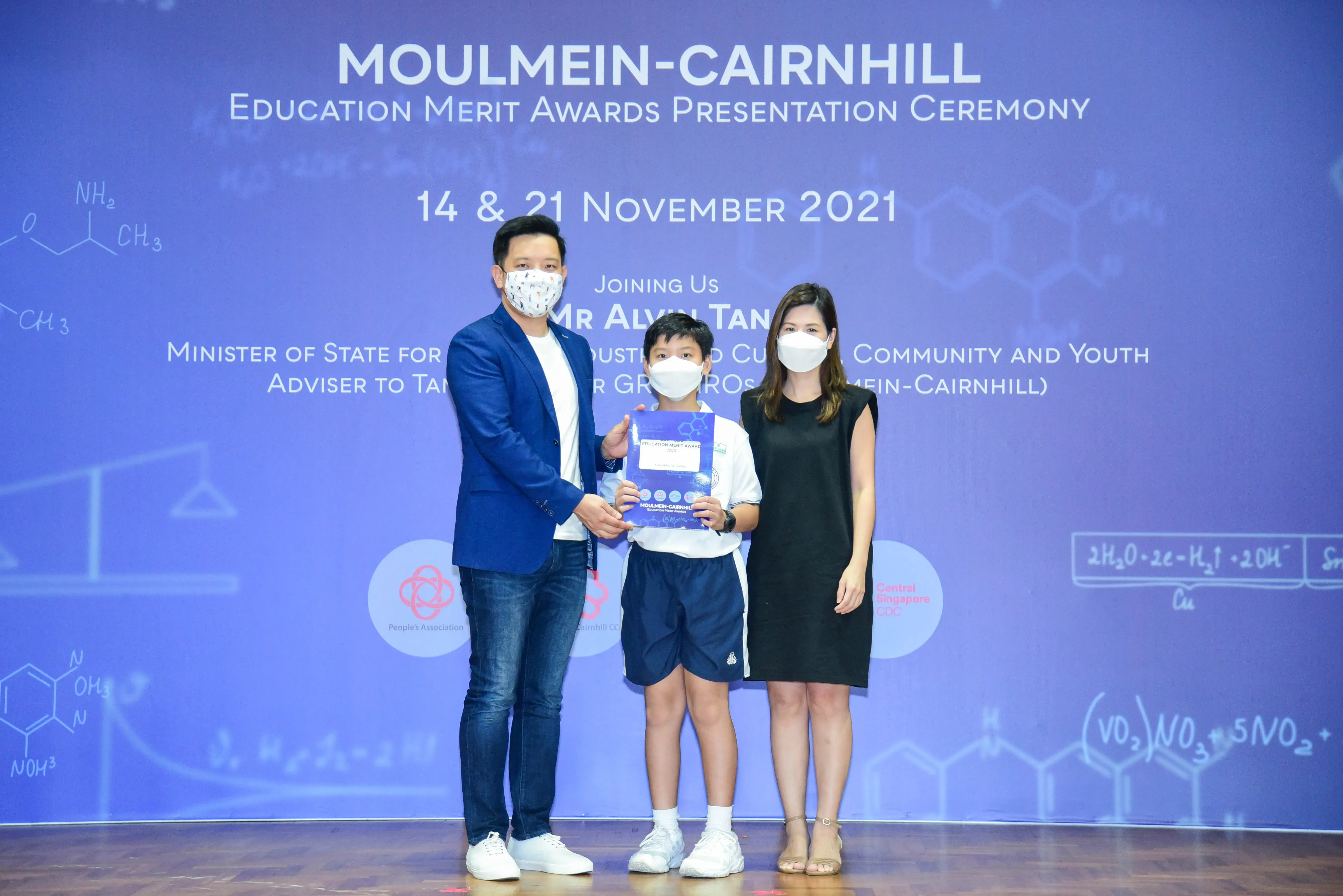 Two masked adults and a masked boy holding an award at the Moulmein-Cairnhill Education Merit Awards ceremony, November 2021.