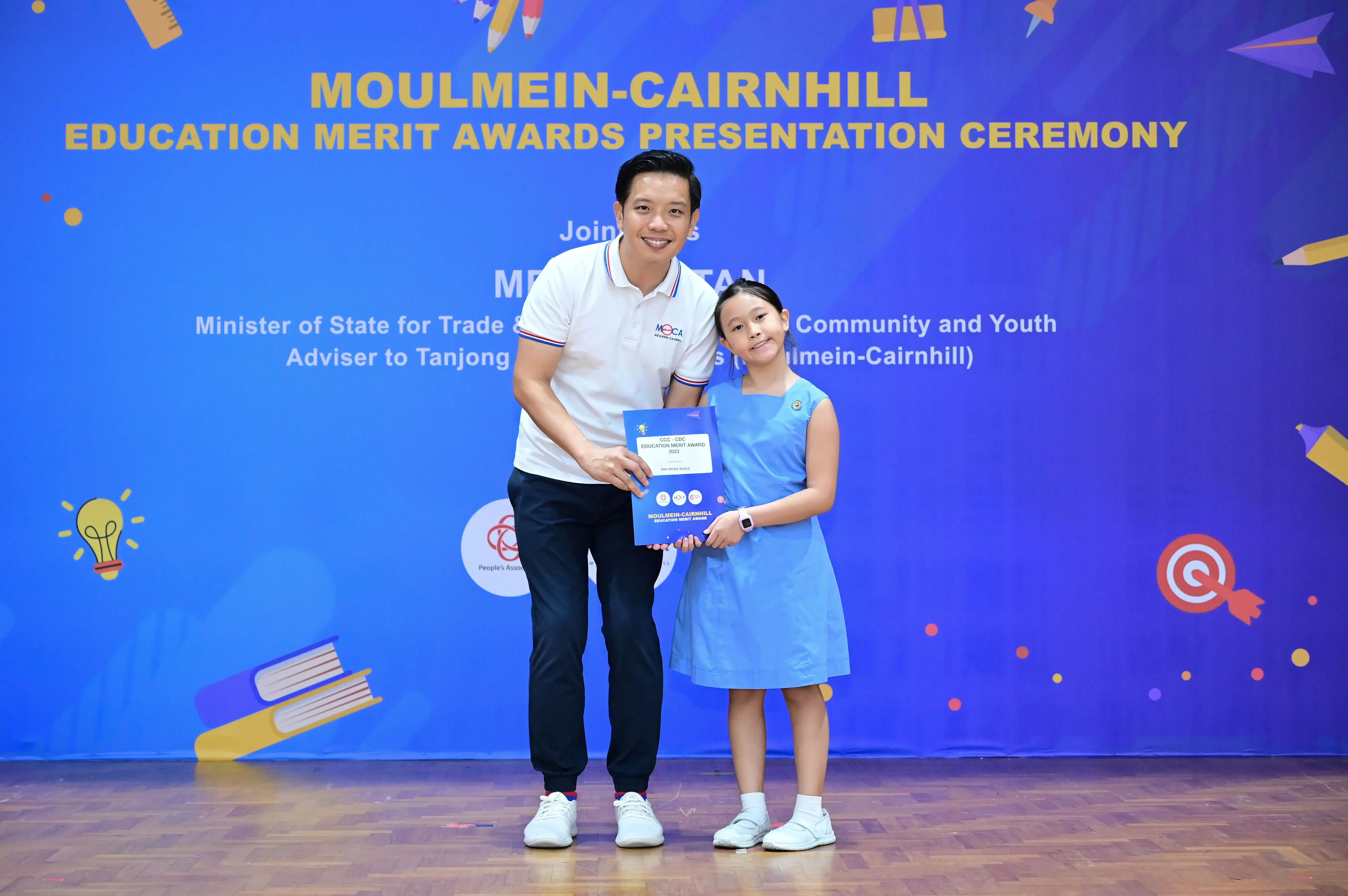 A man and a young girl hold an award certificate at the Moulmein-Cairnhill Education Merit Awards Presentation Ceremony.