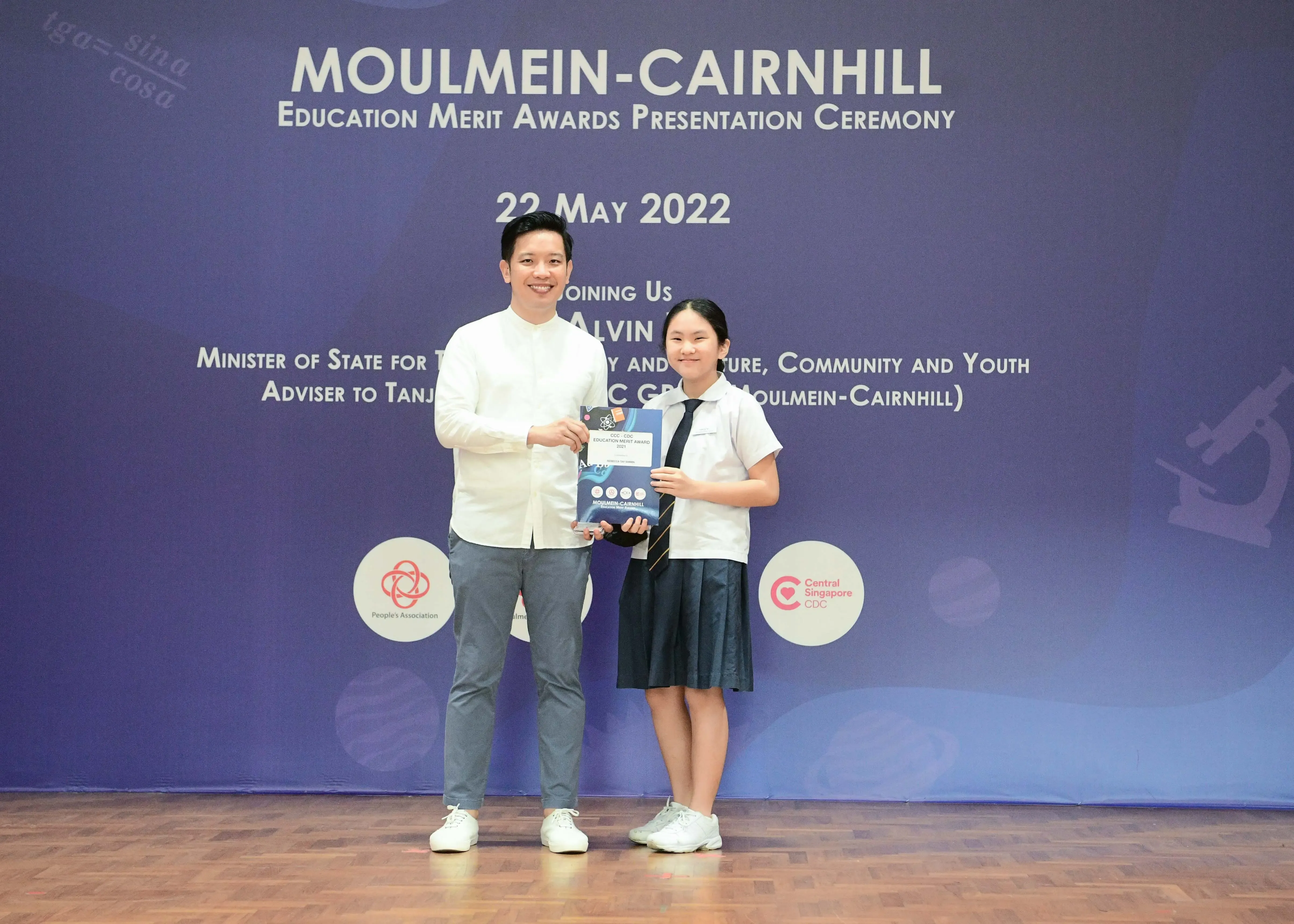 A man and a young girl in school uniform hold an award together at the Moulmein-Cairnhill Education Merit Awards on 22 May 2022.