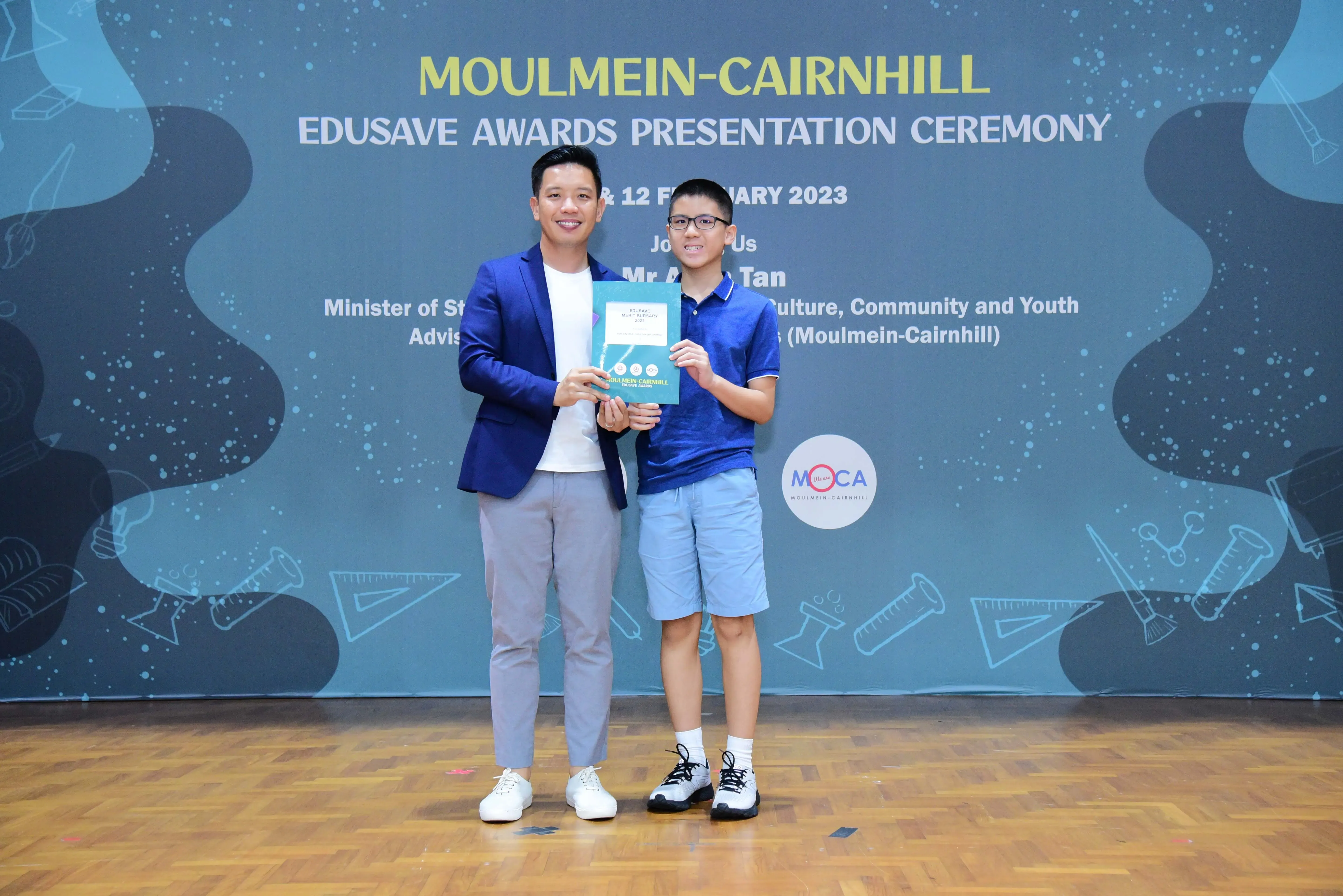 Two people pose holding an award folder at the Moulmein-Cairnhill Edusave Awards Presentation Ceremony 2023.