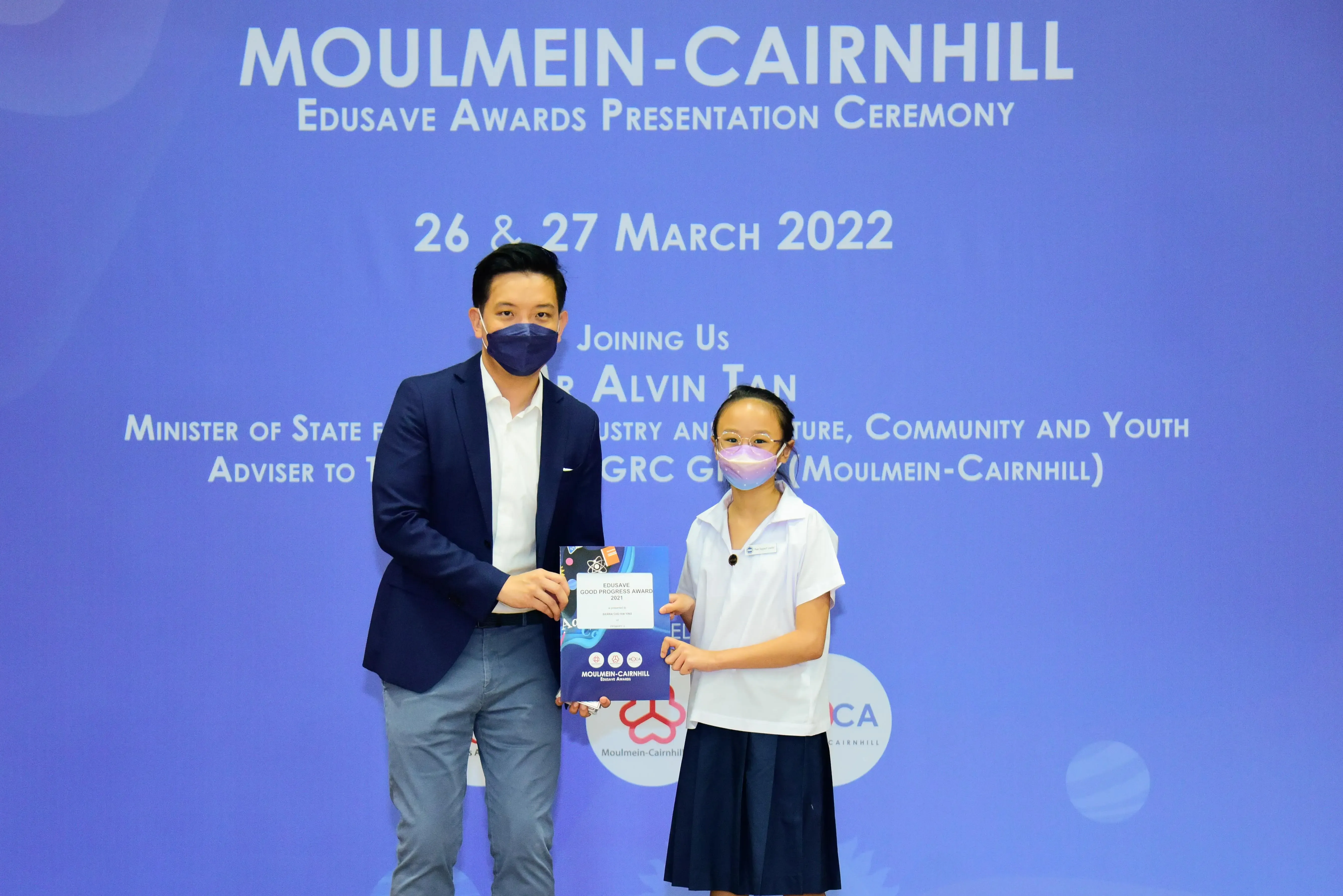 A man and a young girl in school uniform hold an award at the Moulmein-Cairnhill Edusave Awards Ceremony, March 2022.