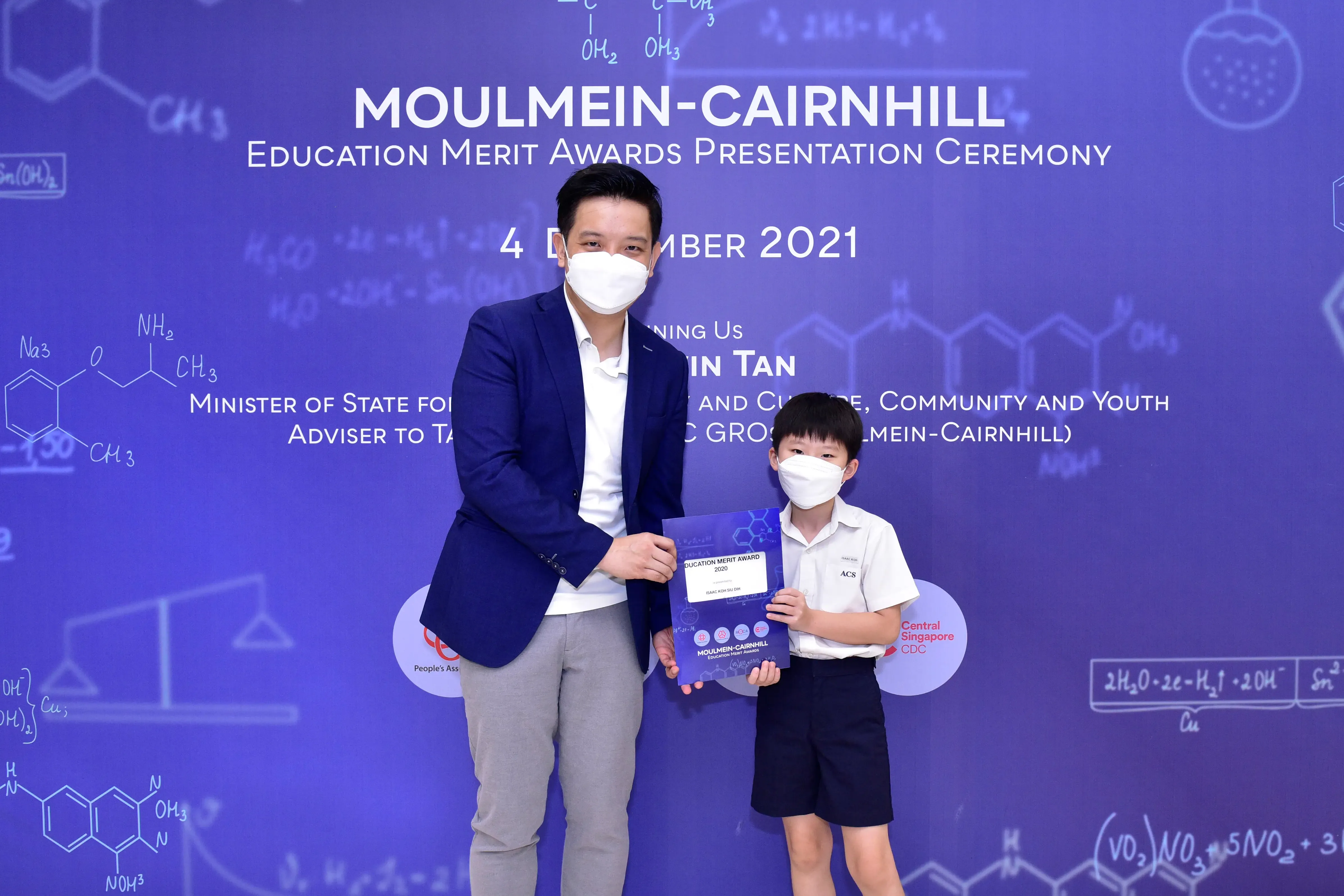 An adult and a young boy wearing masks hold a certificate at the Moulmein-Cairnhill Education Merit Awards 2021.