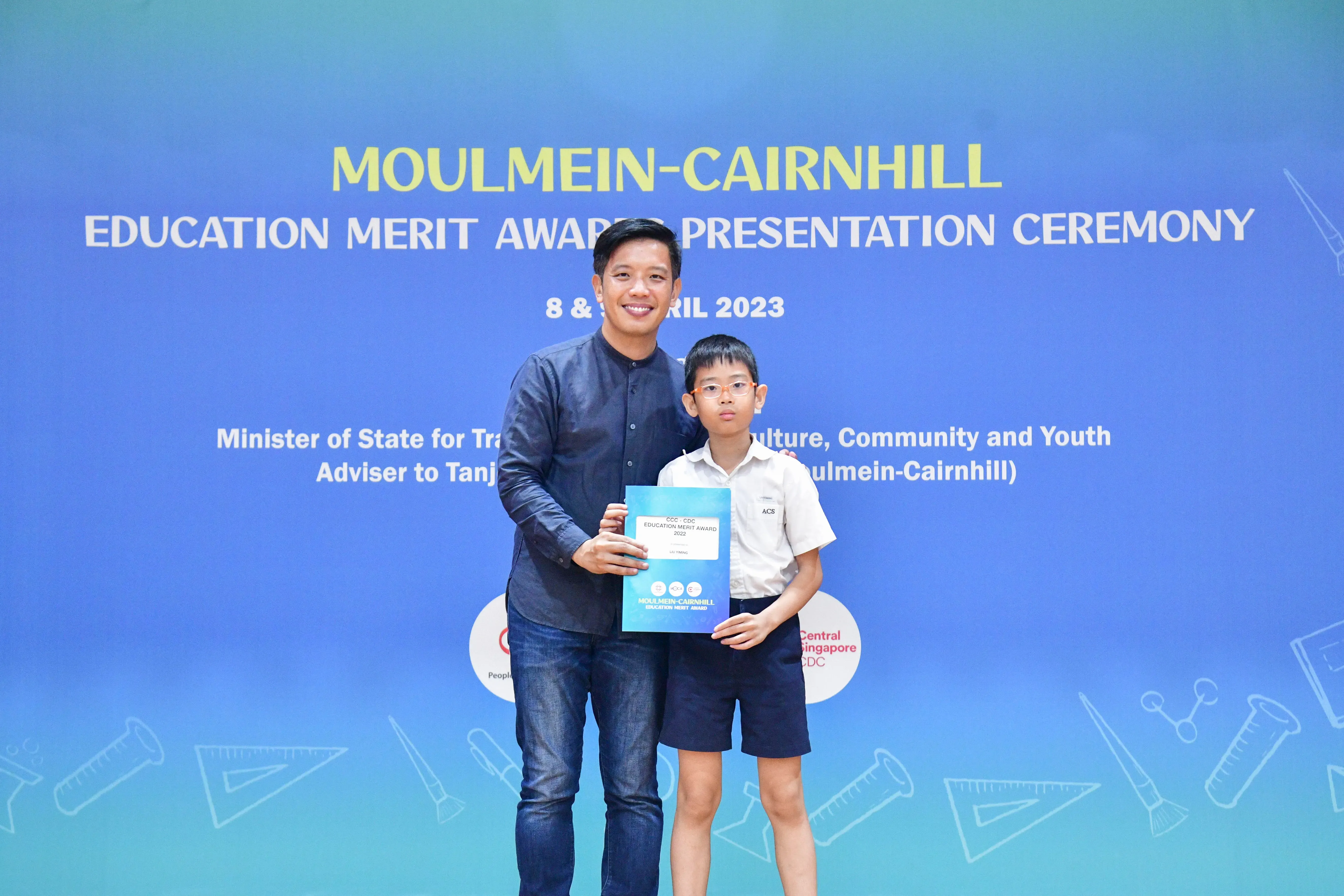Man and young boy holding a certificate at the Moulmein-Cairnhill Education Merit Award Ceremony, April 2023.