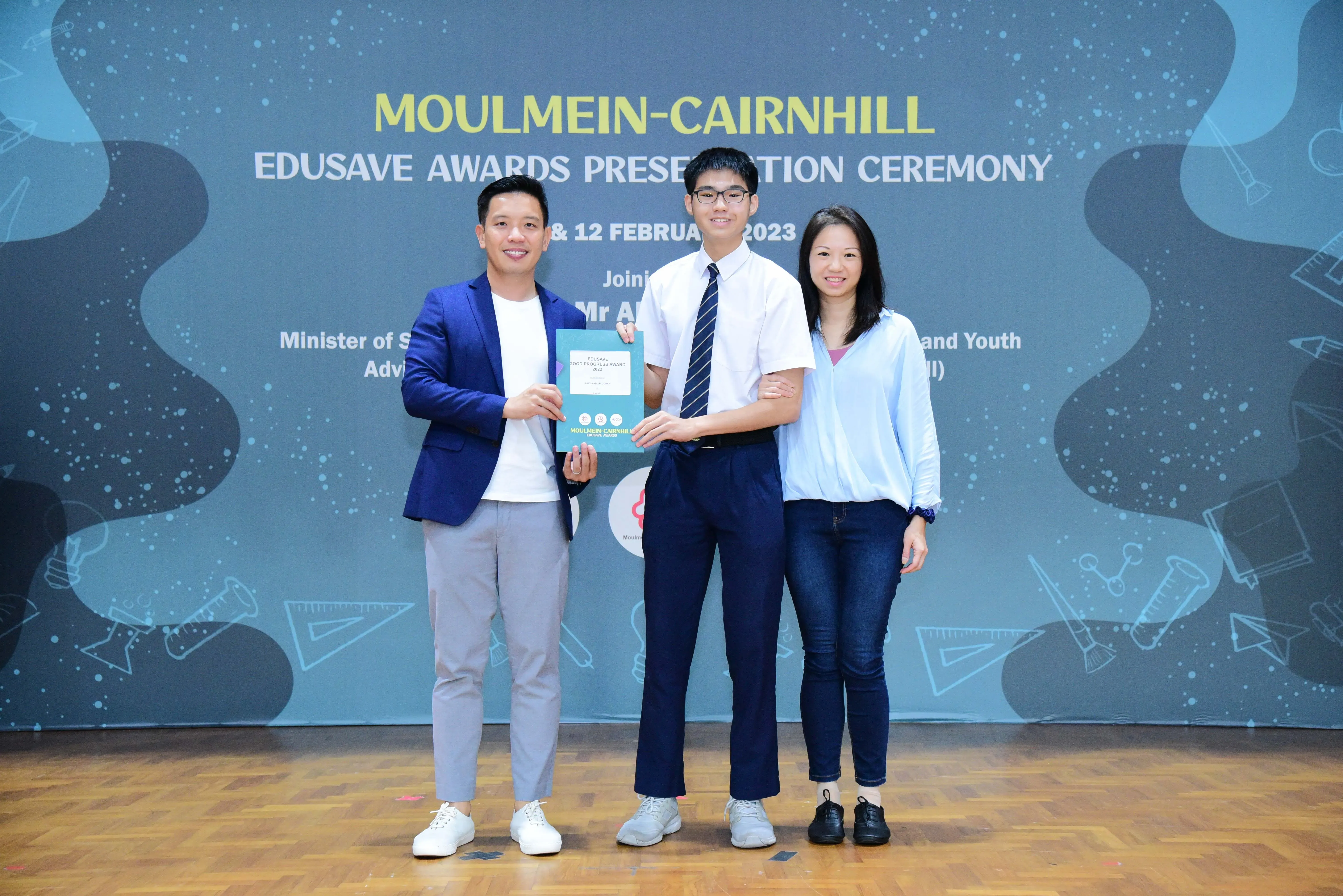 Three people smile holding an award certificate at the Moulmein-Cairnhill Edusave Awards Presentation Ceremony 2023.