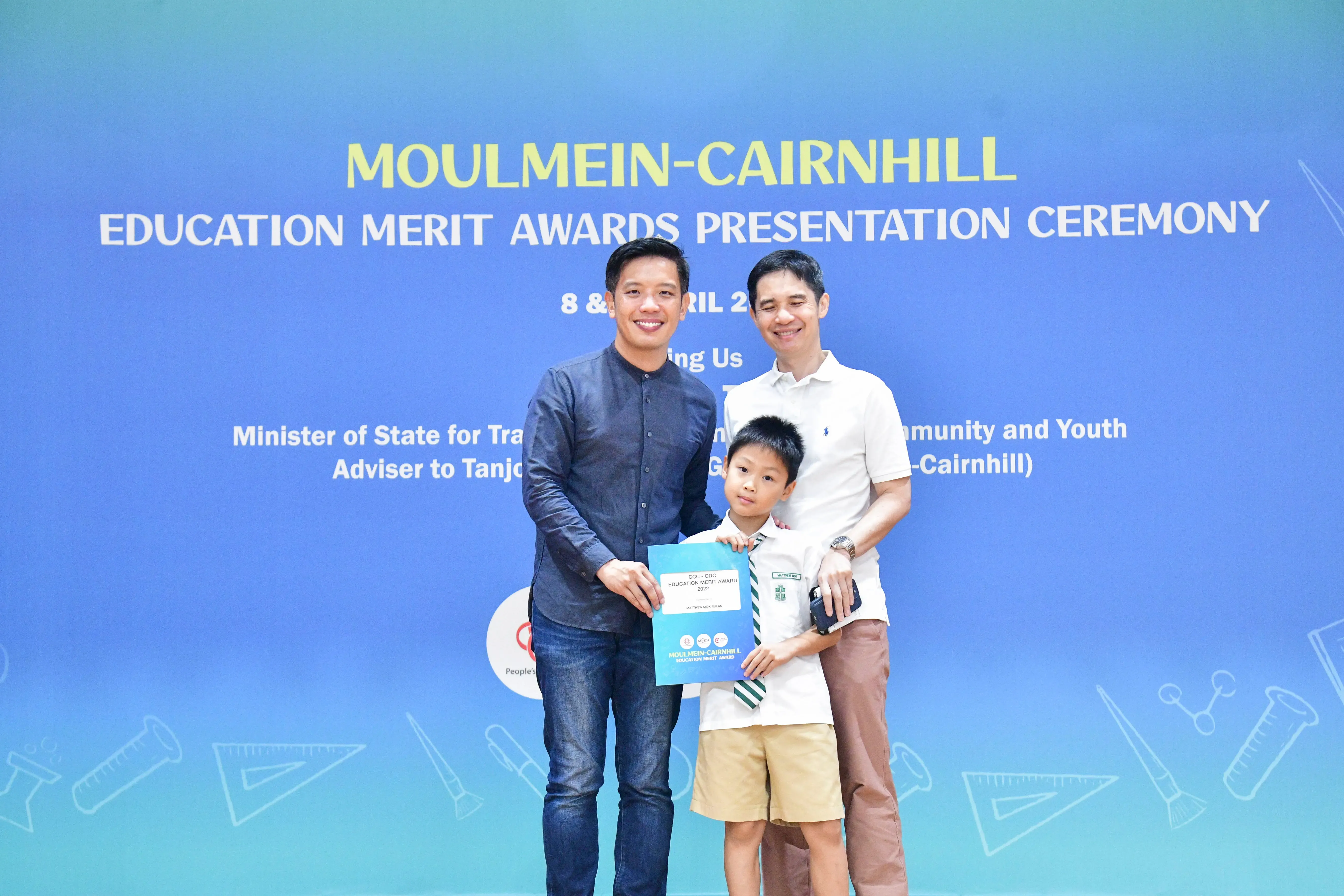 Two men and a young boy pose with a certificate at the Moulmein-Cairnhill Education Merit Awards ceremony.