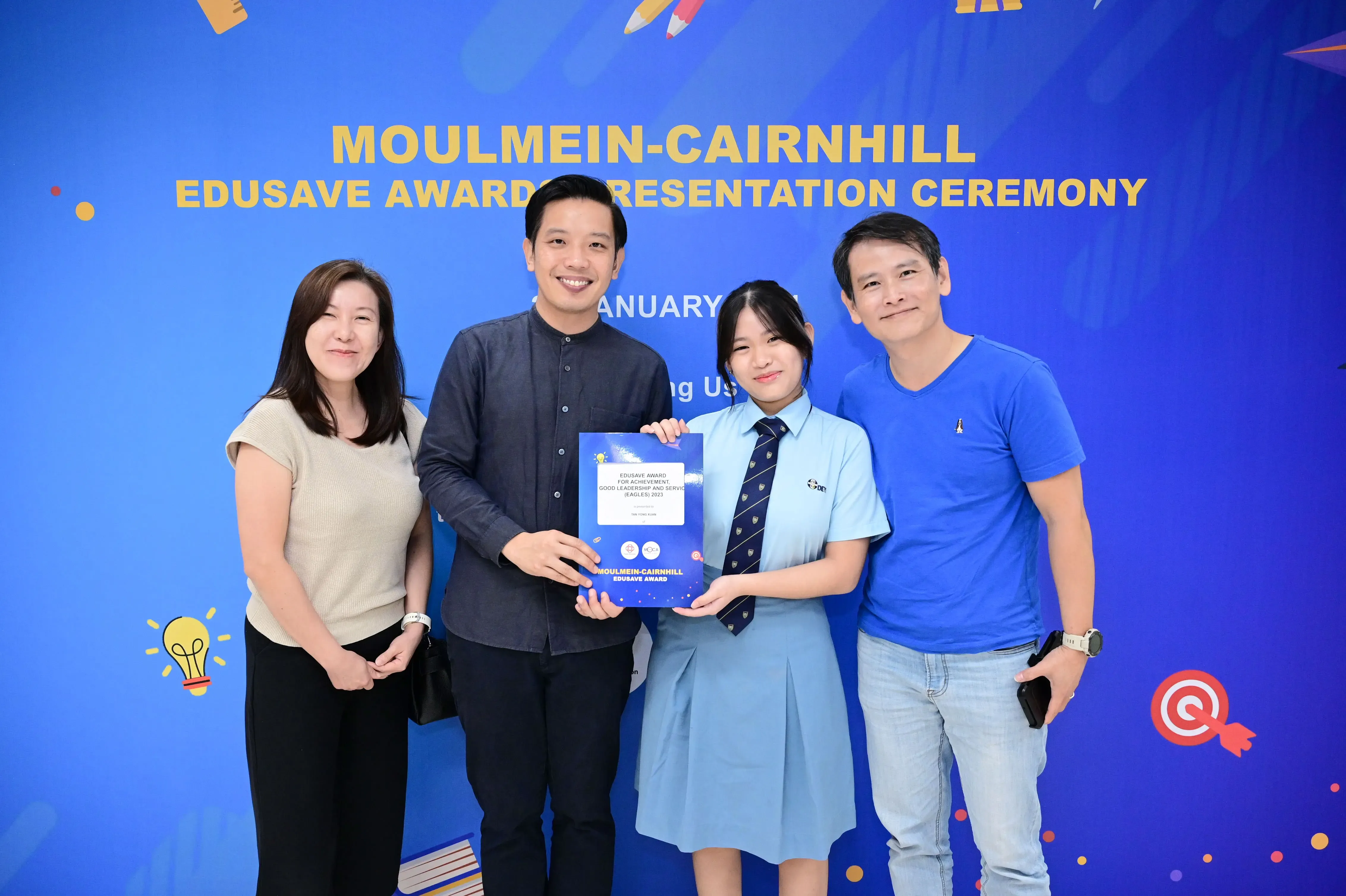Four people pose at the Moulmein-Cairnhill Edusave Awards Ceremony, with a student holding an award certificate.