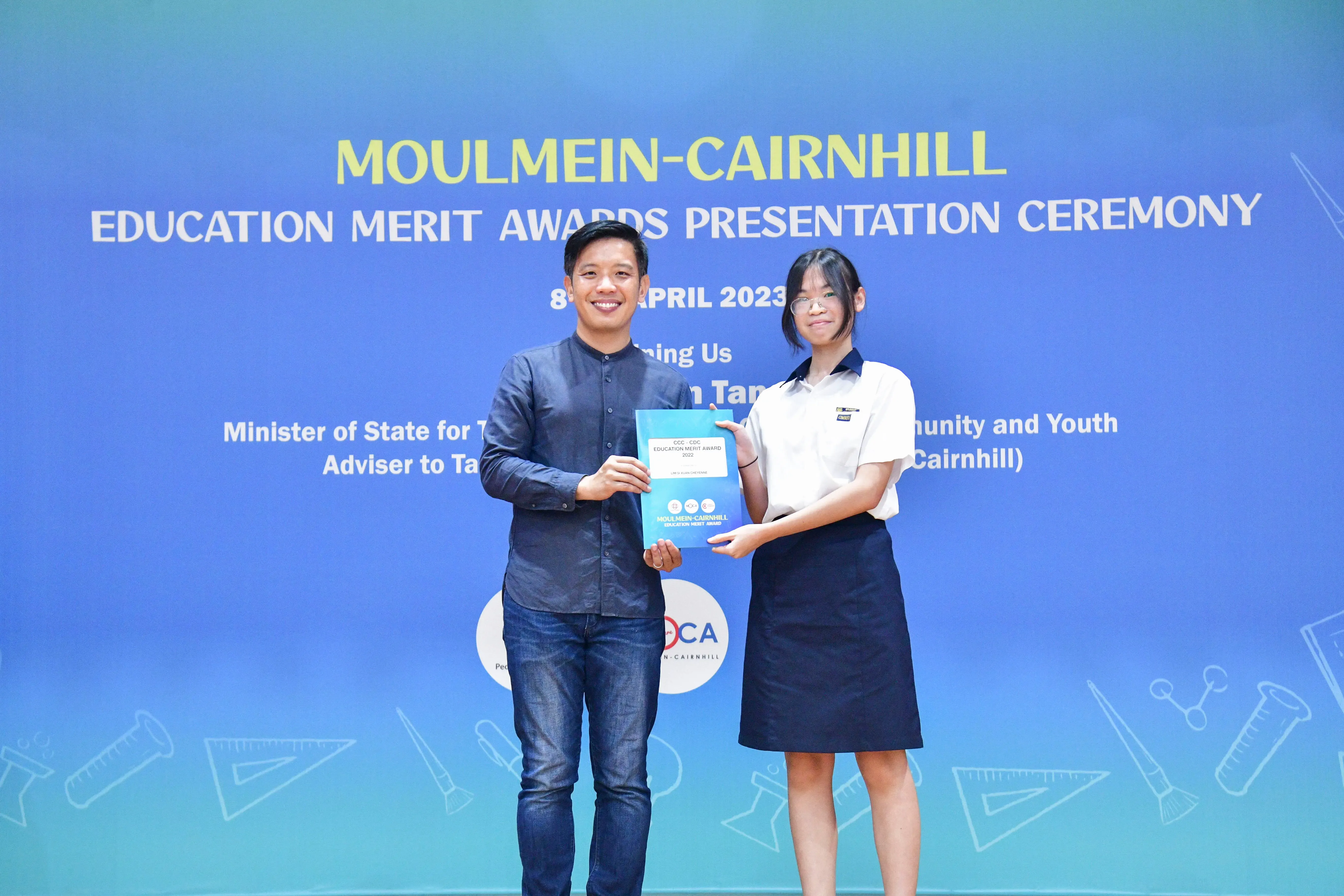 Two people hold a certificate together at the Moulmein-Cairnhill Education Merit Awards Presentation Ceremony, April 2023.