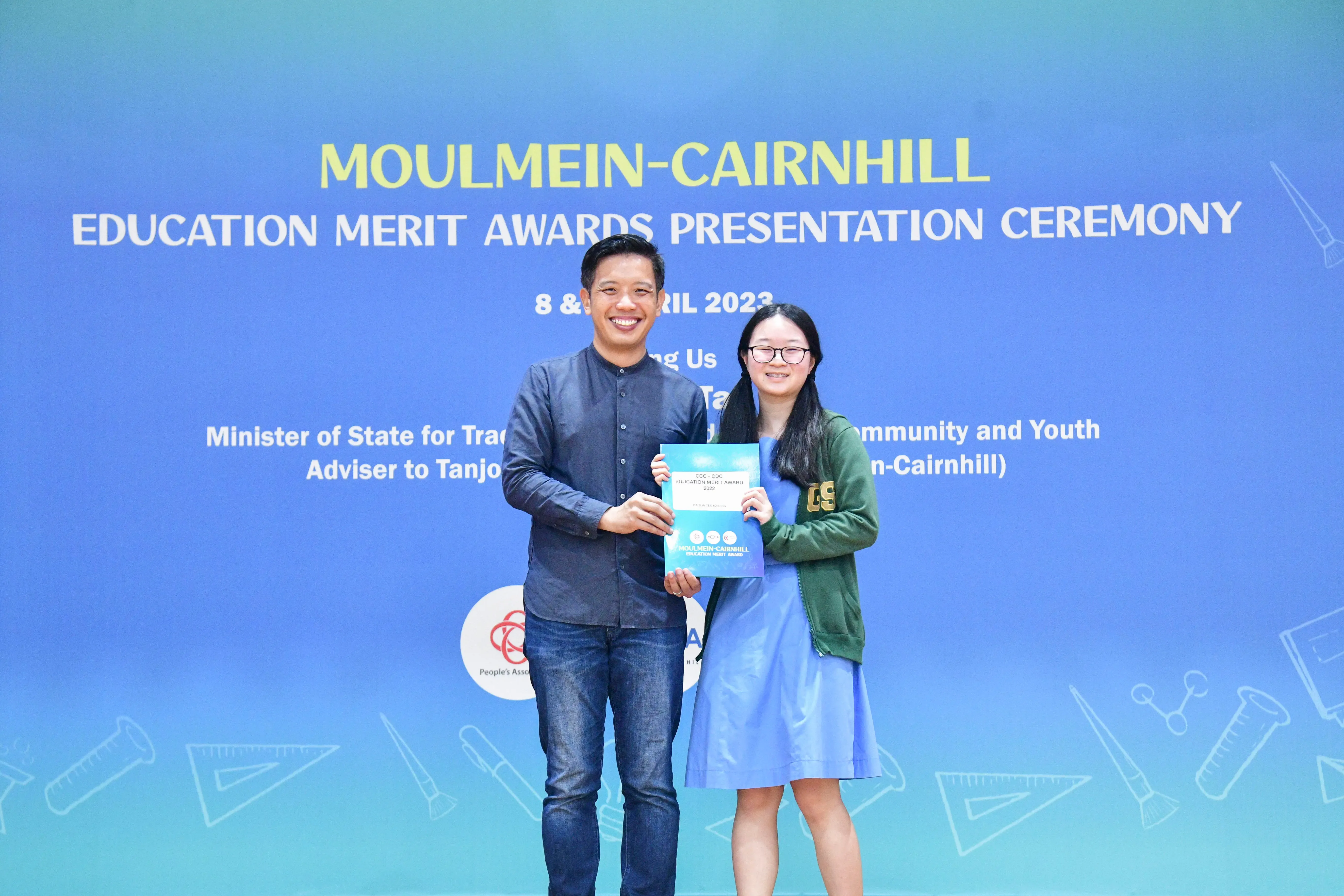 Two people smile while holding an award certificate at the Moulmein-Cairnhill Education Merit Awards Ceremony, April 2023.