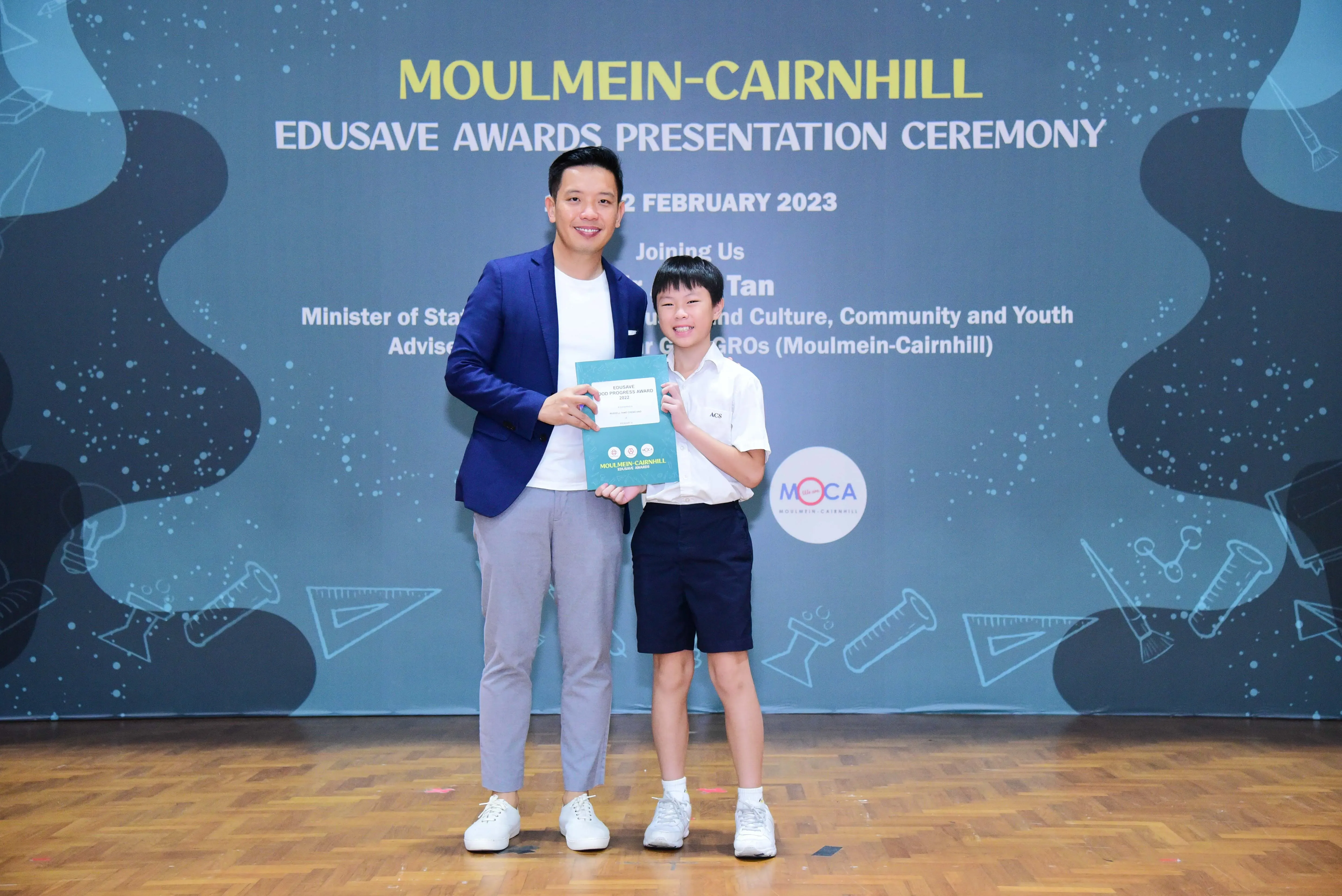 A man and a young boy hold an award booklet at the Moulmein-Cairnhill Edusave Awards Ceremony, February 2023.