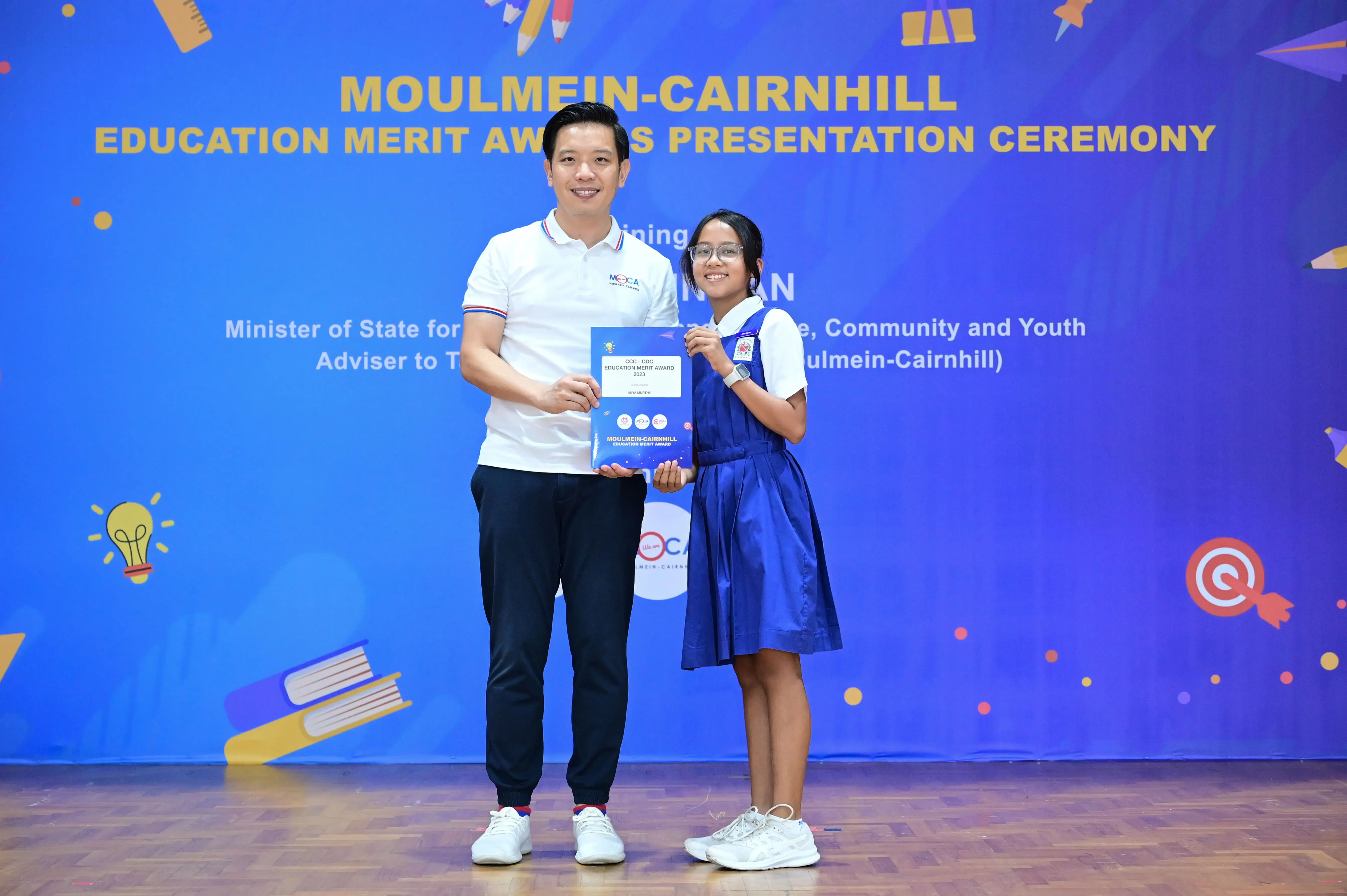 A man and a young girl in school uniform hold a certificate at the Moulmein-Cairnhill Education Merit Awards ceremony.