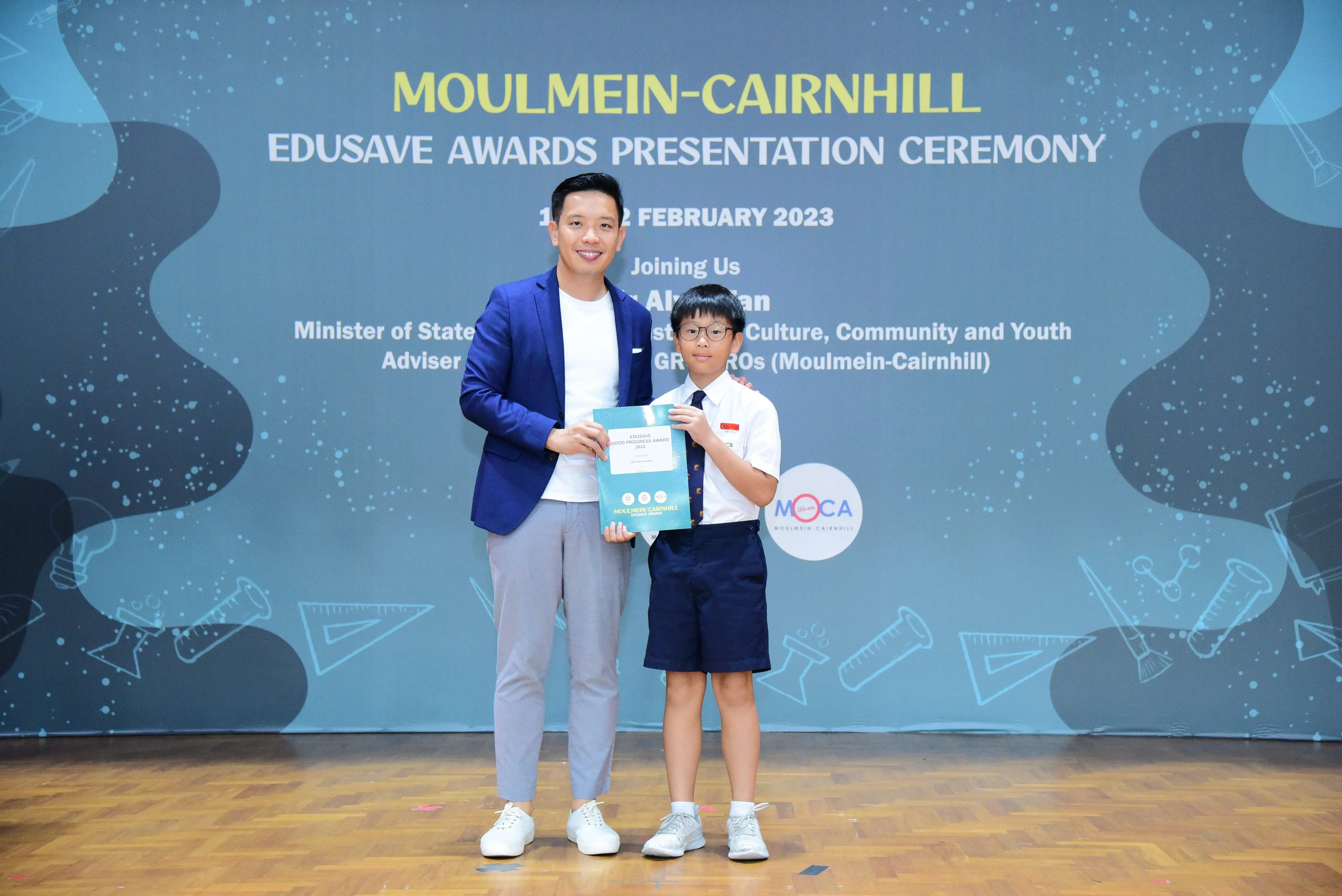 An adult and a young student hold a certificate at the Moulmein-Cairnhill Edusave Awards Ceremony, February 2023.