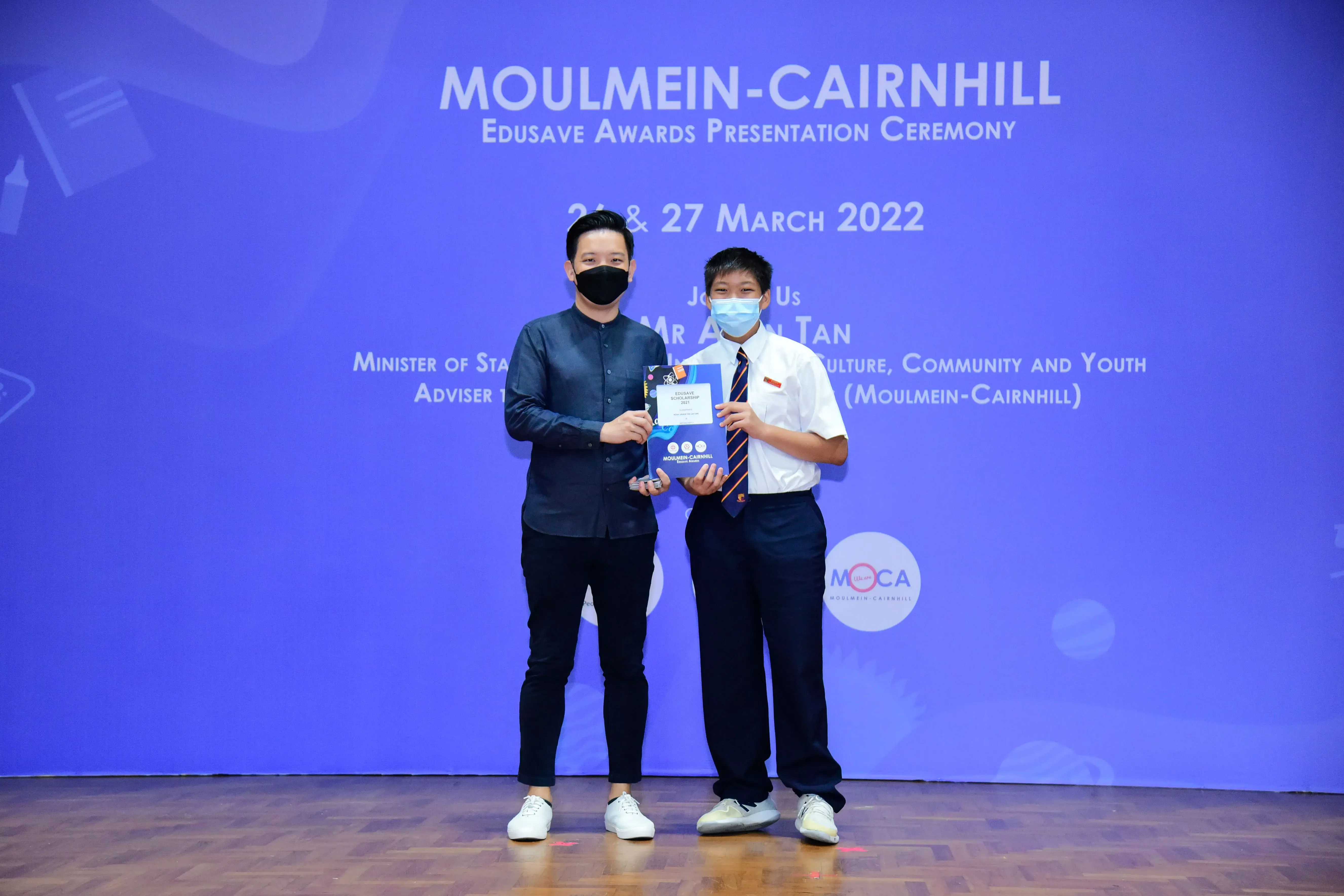 Two masked individuals hold an award booklet at the Moulmein-Cairnhill Edusave Awards Ceremony, March 2022.