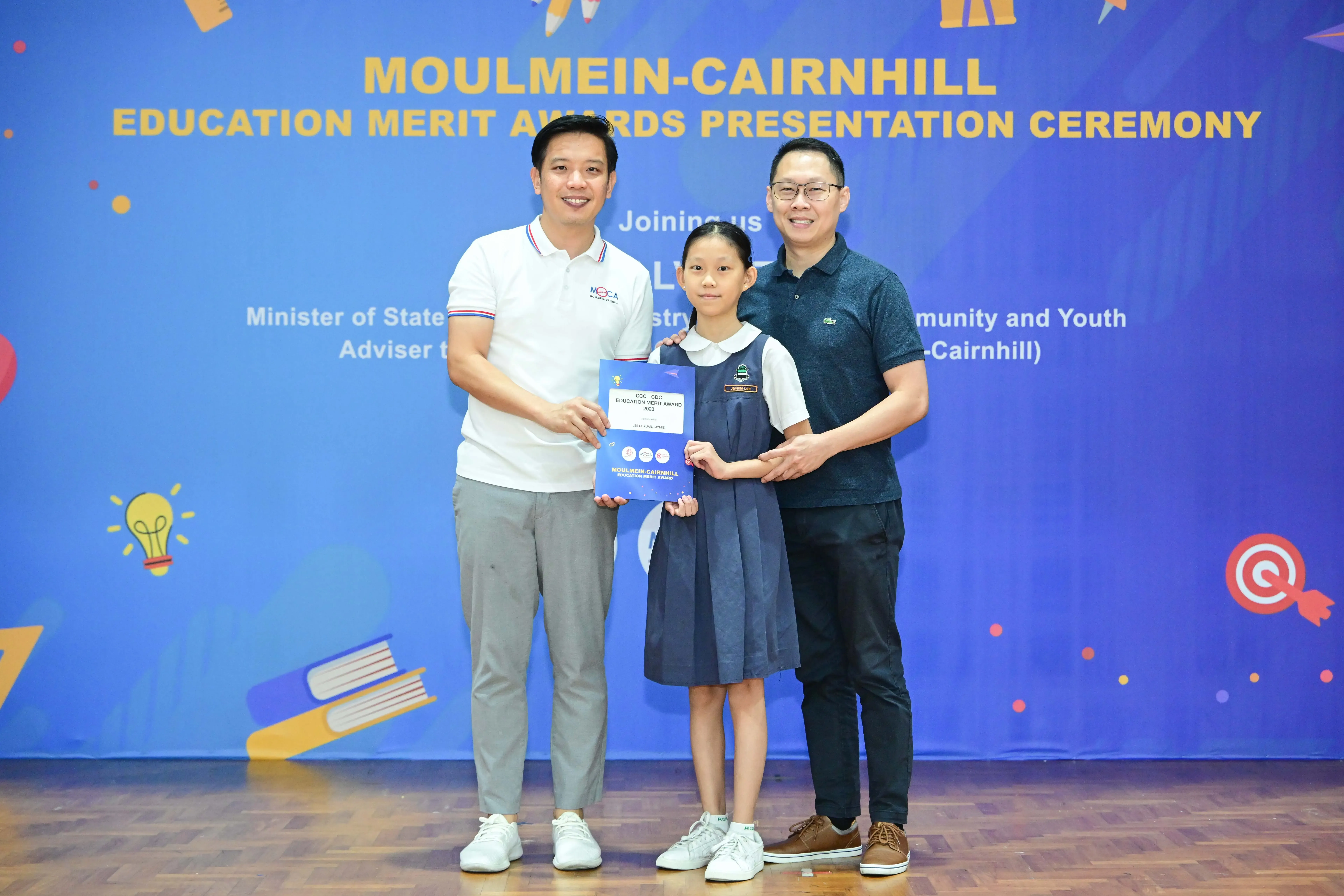 Two men and a young girl in school uniform hold a certificate at the Moulmein-Cairnhill Education Merit Awards ceremony.