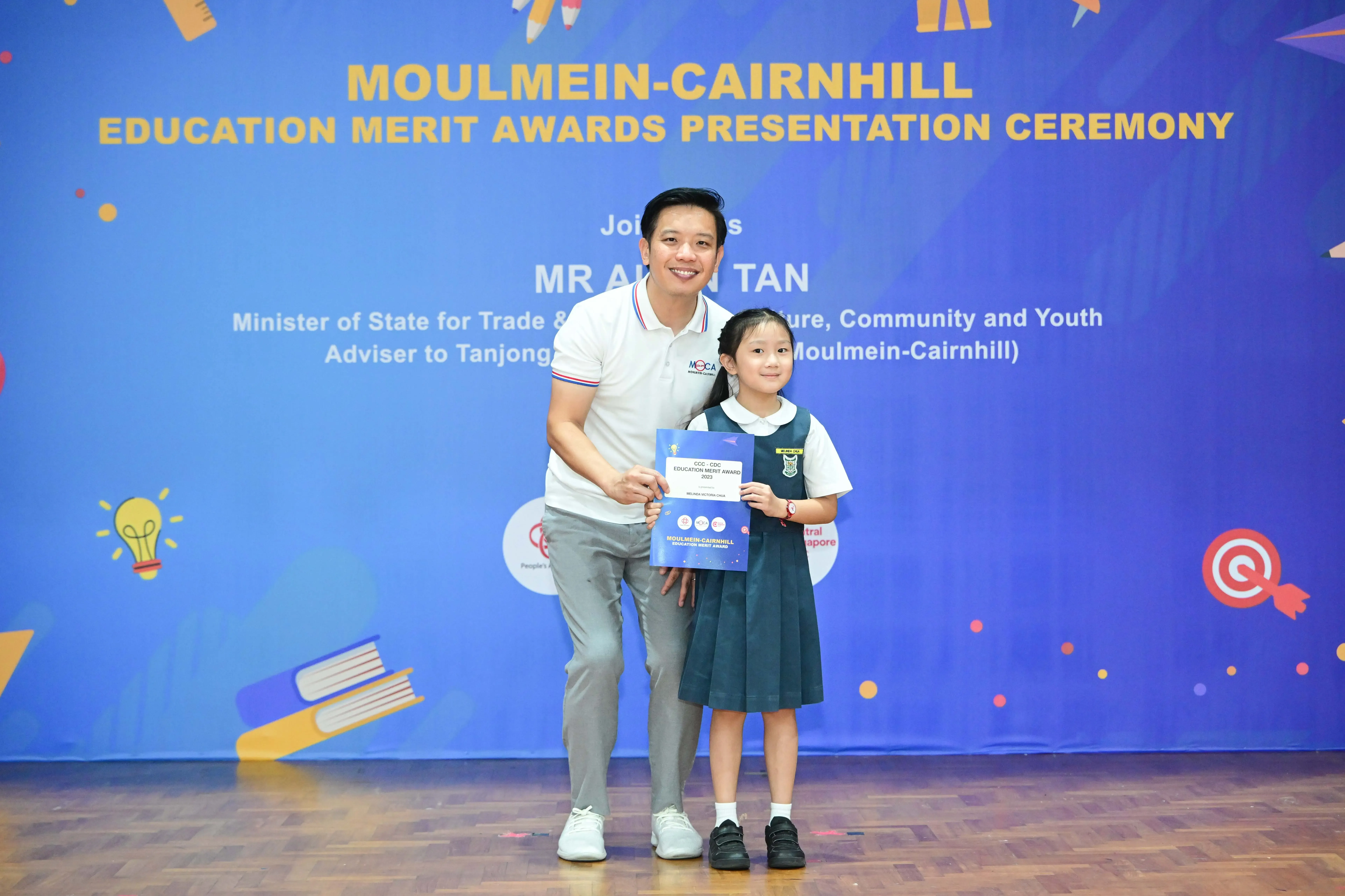 A man and a young girl in school uniform pose together holding an award certificate at the Moulmein-Cairnhill Education Merit Awards ceremony.
