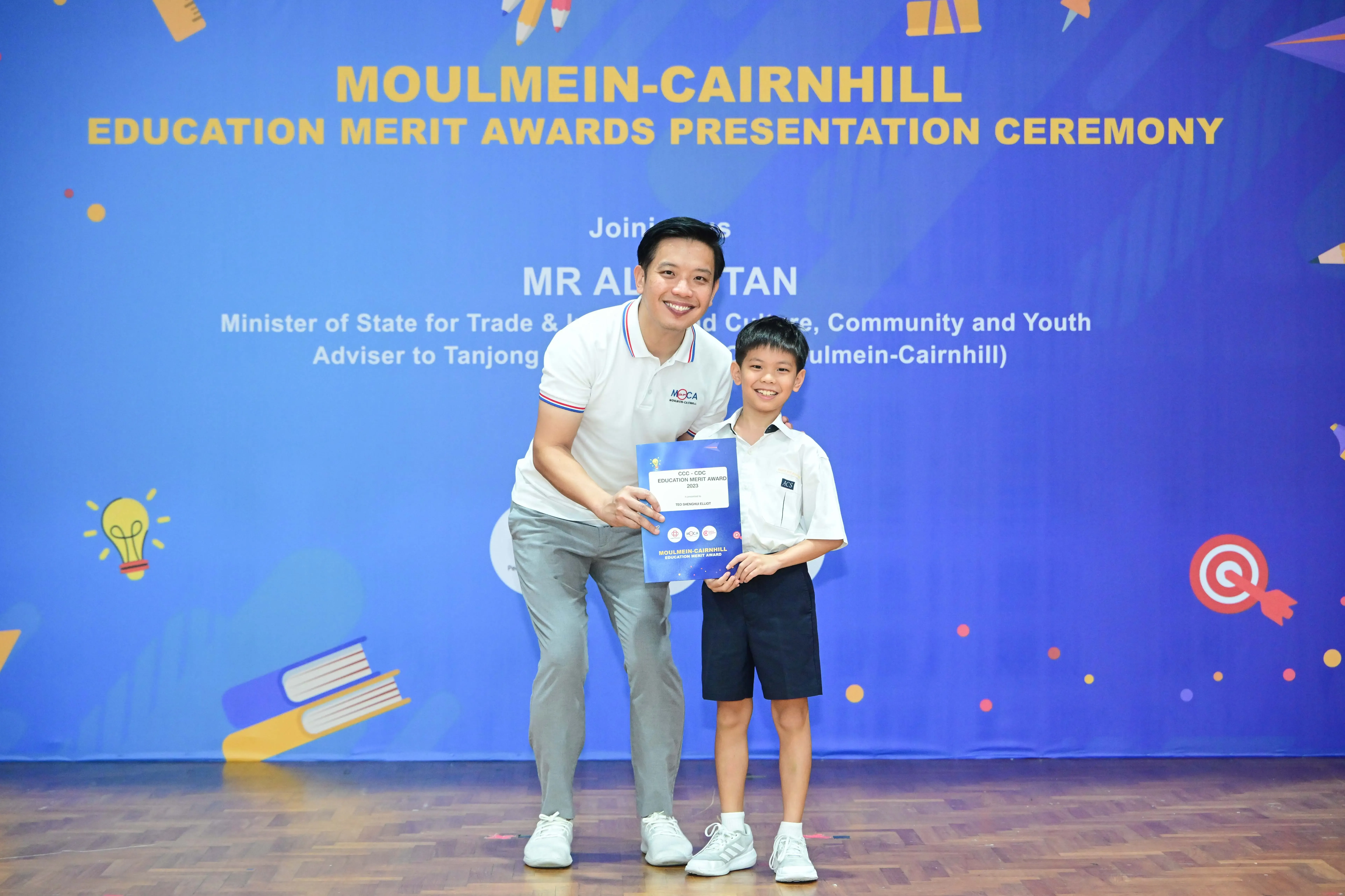 A man and a young boy pose together holding an award certificate at the Moulmein-Cairnhill Education Merit Awards ceremony.
