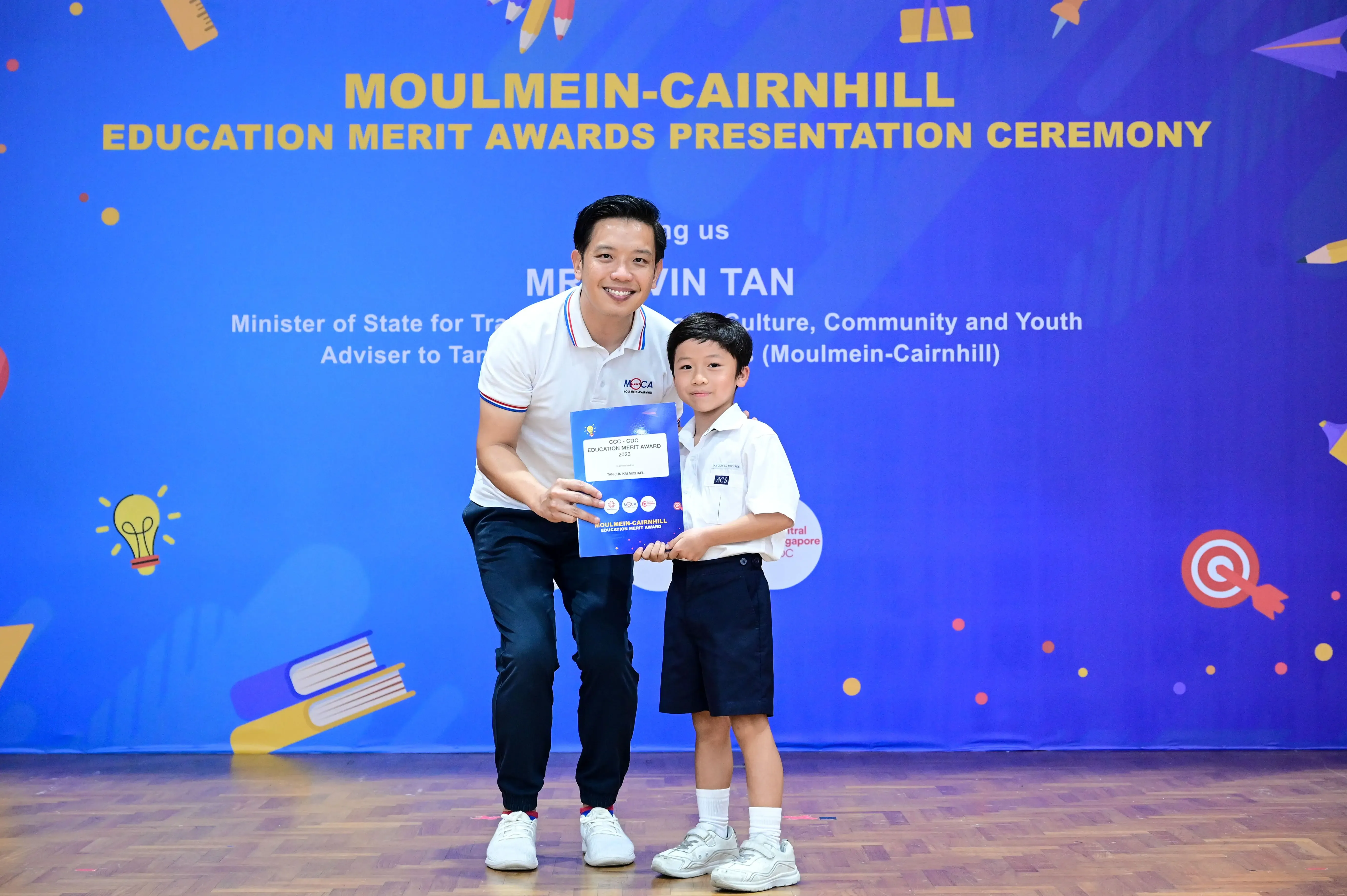 A man and a young boy hold an award certificate at the Moulmein-Cairnhill Education Merit Awards Presentation Ceremony.