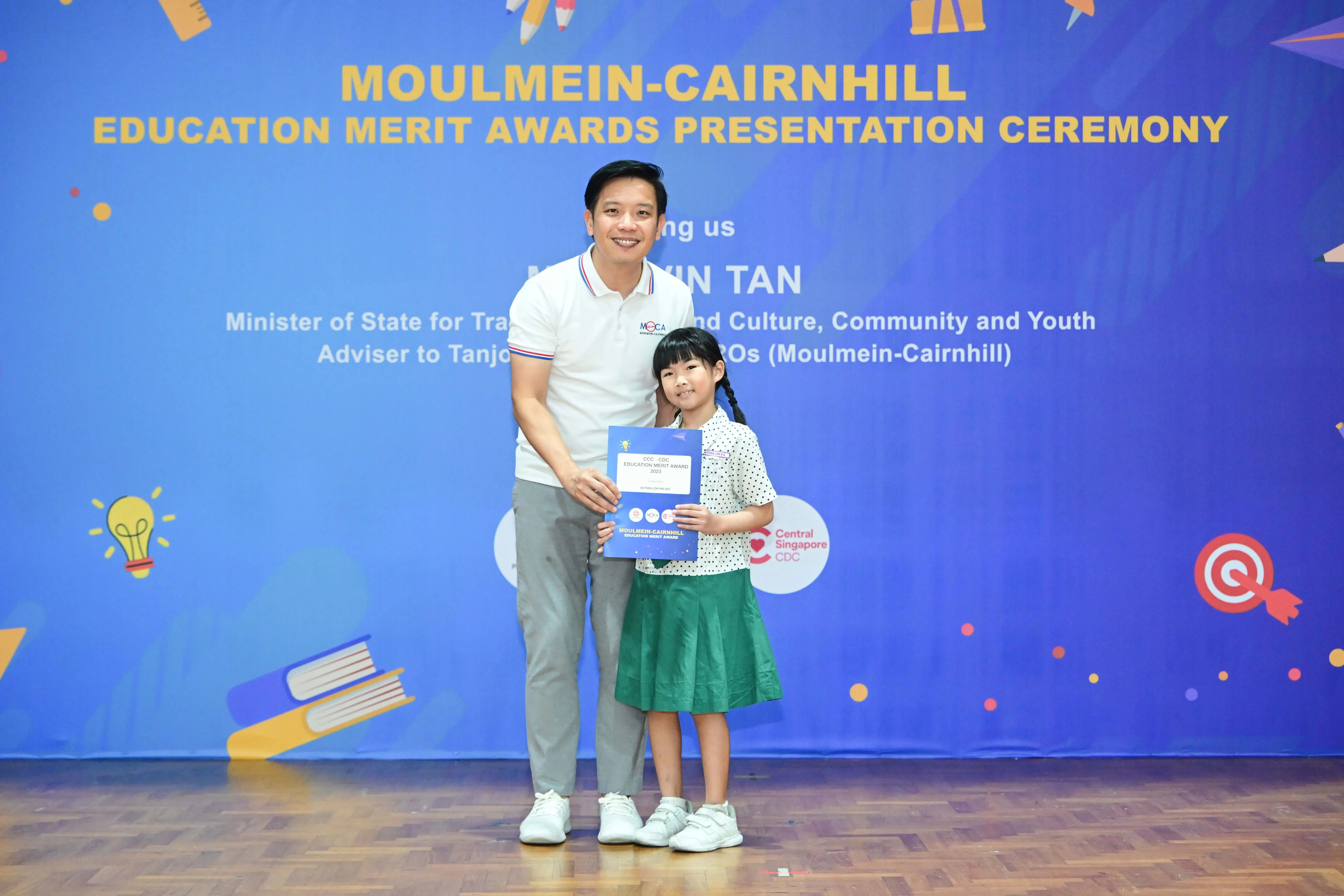 A man and a young girl hold a certificate at the Moulmein-Cairnhill Education Merit Awards Presentation Ceremony.