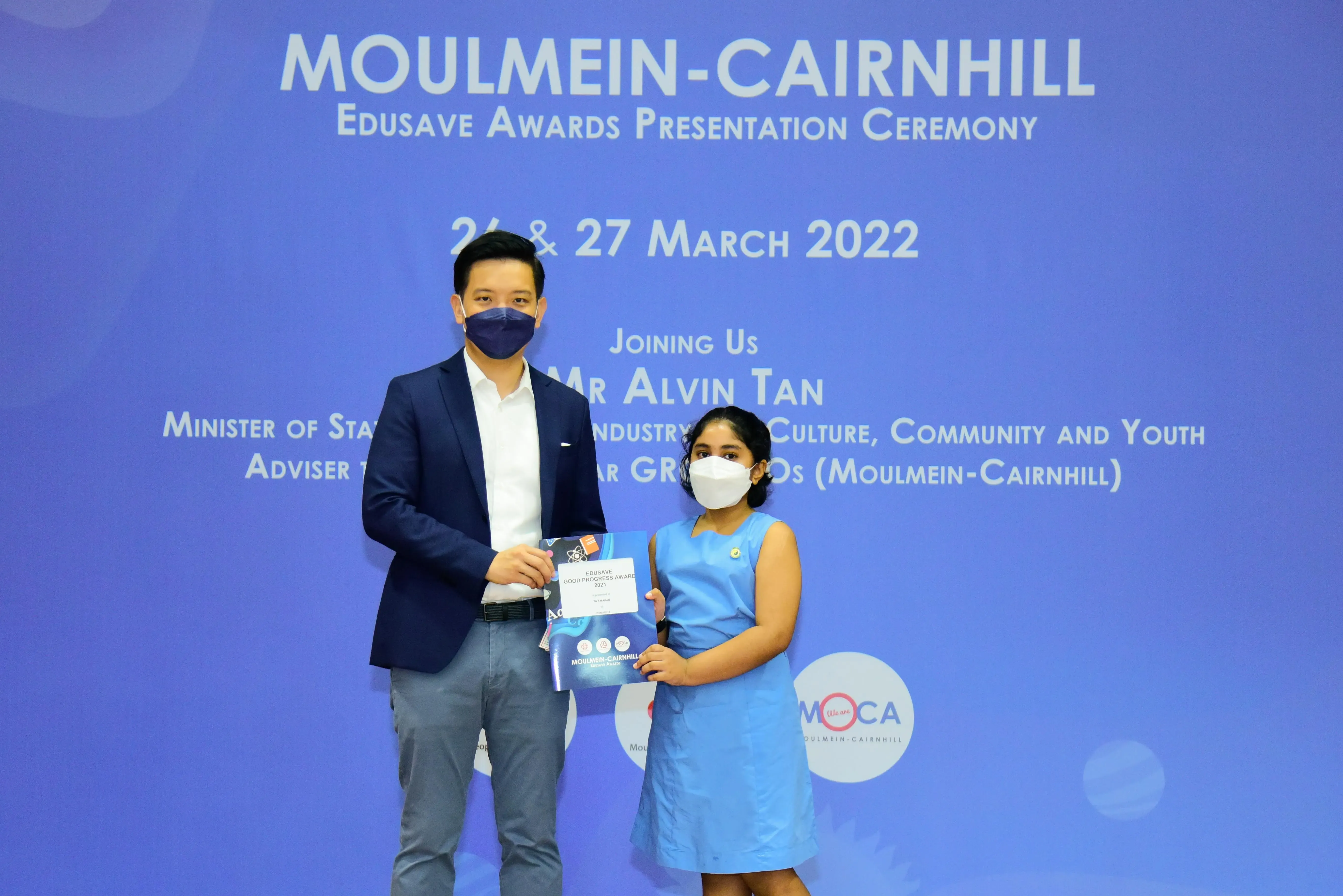 A masked man and young girl hold a certificate at the Moulmein-Cairnhill Edusave Awards Ceremony, March 2022.