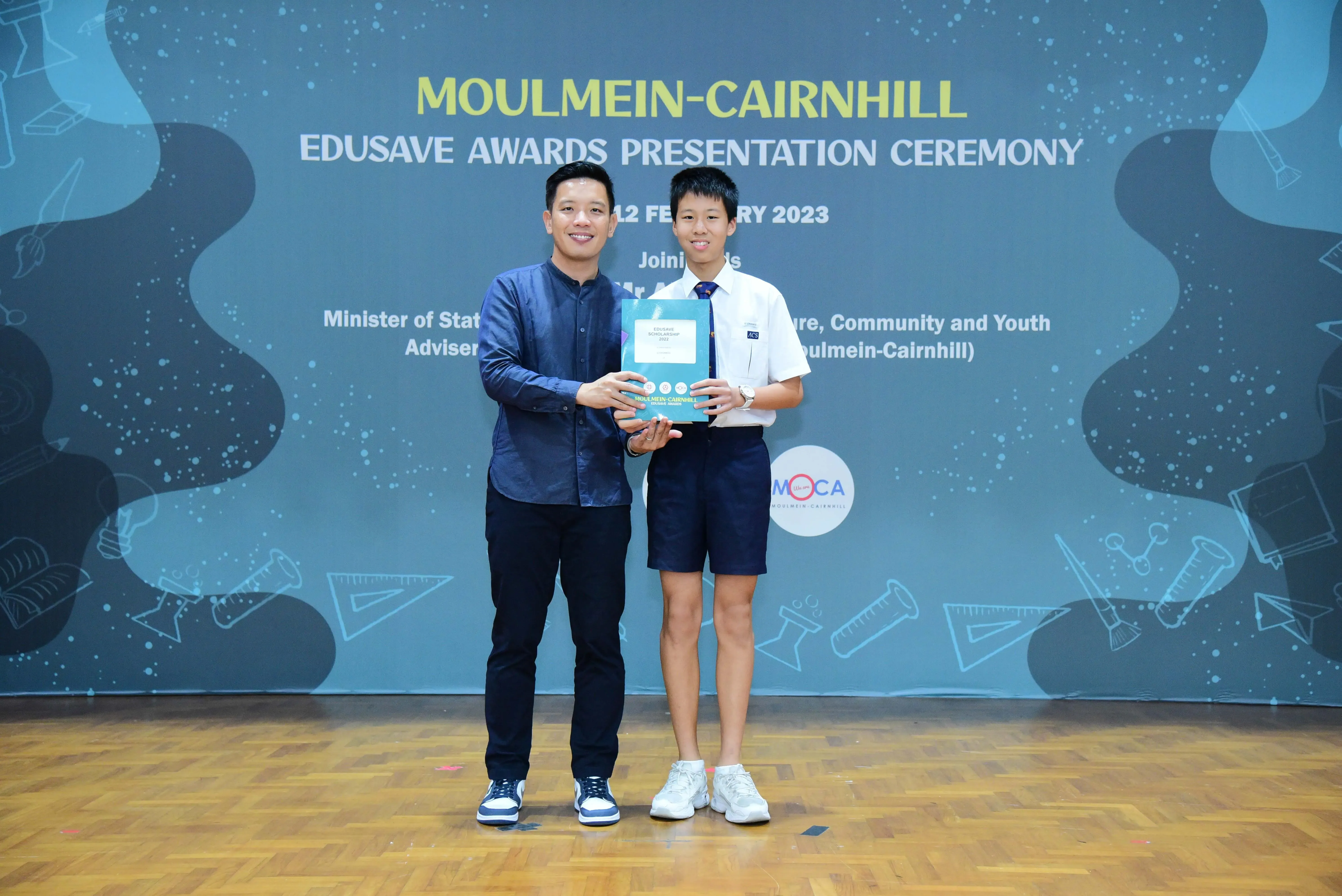 Two people smile holding an award booklet at the Moulmein-Cairnhill Edusave Awards Presentation Ceremony 2023.