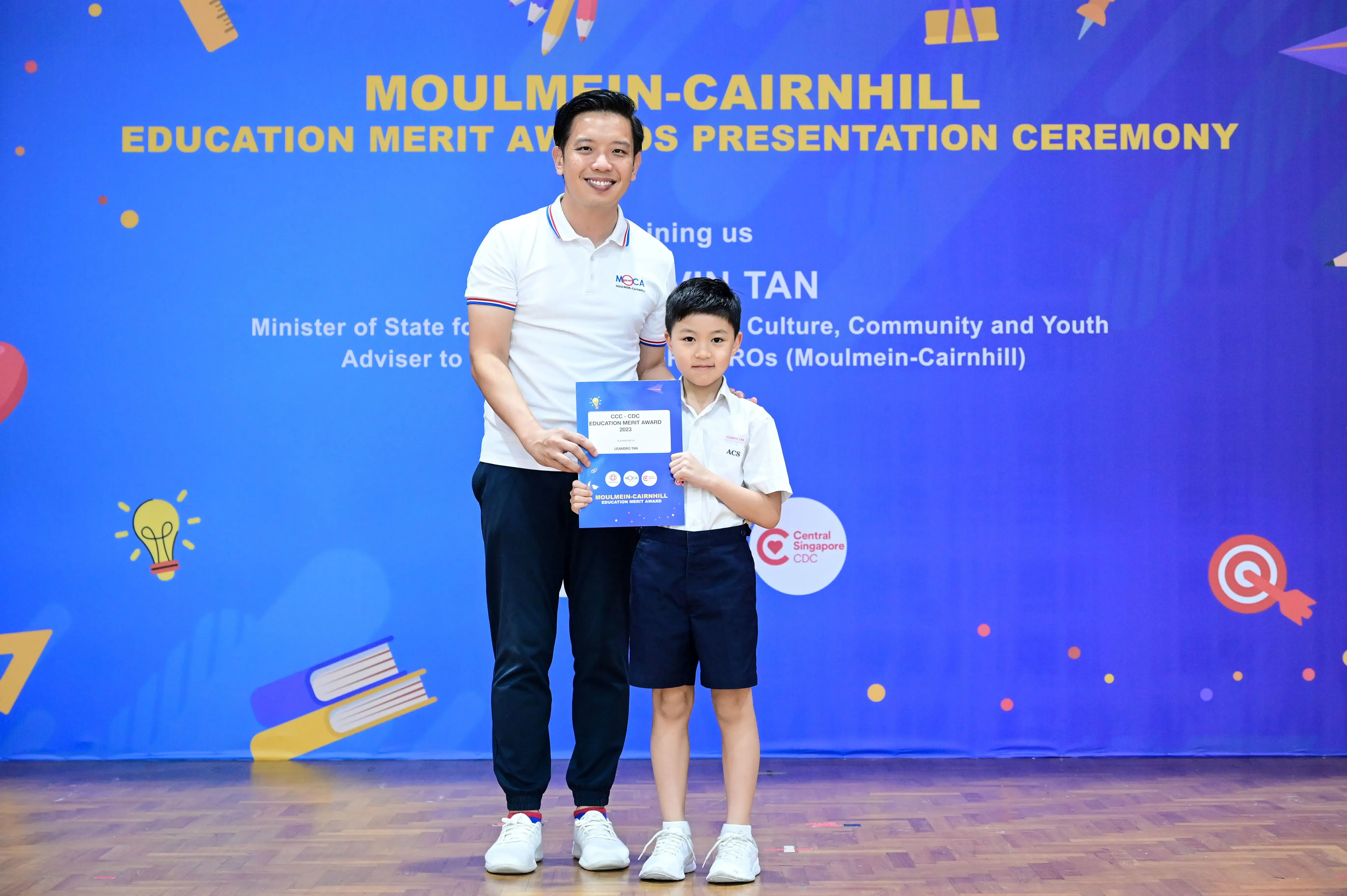 Adult and young boy holding a certificate at the Moulmein-Cairnhill Education Merit Awards Presentation Ceremony.