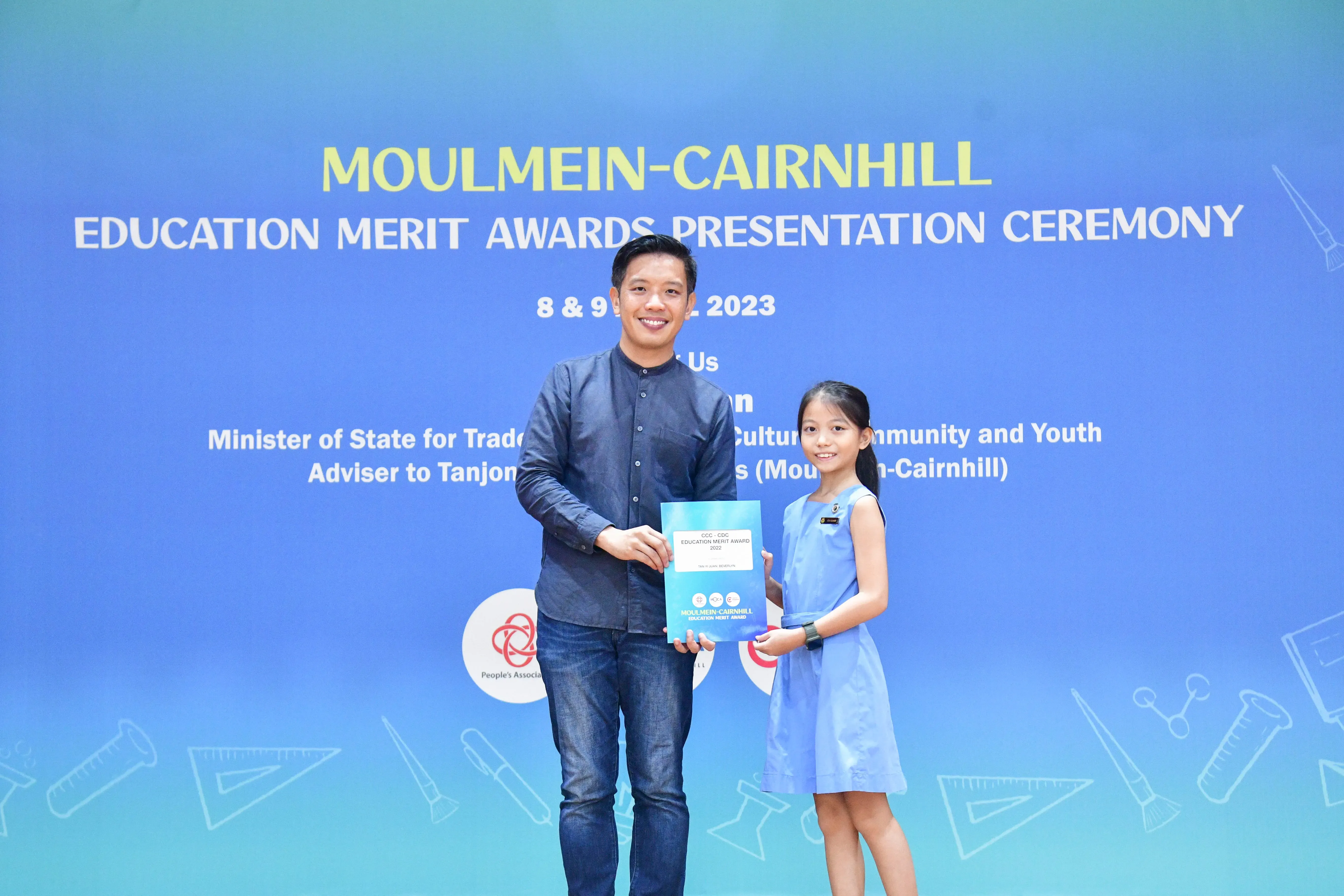 A man and a young girl hold an award certificate at the Moulmein-Cairnhill Education Merit Awards Ceremony 2023.