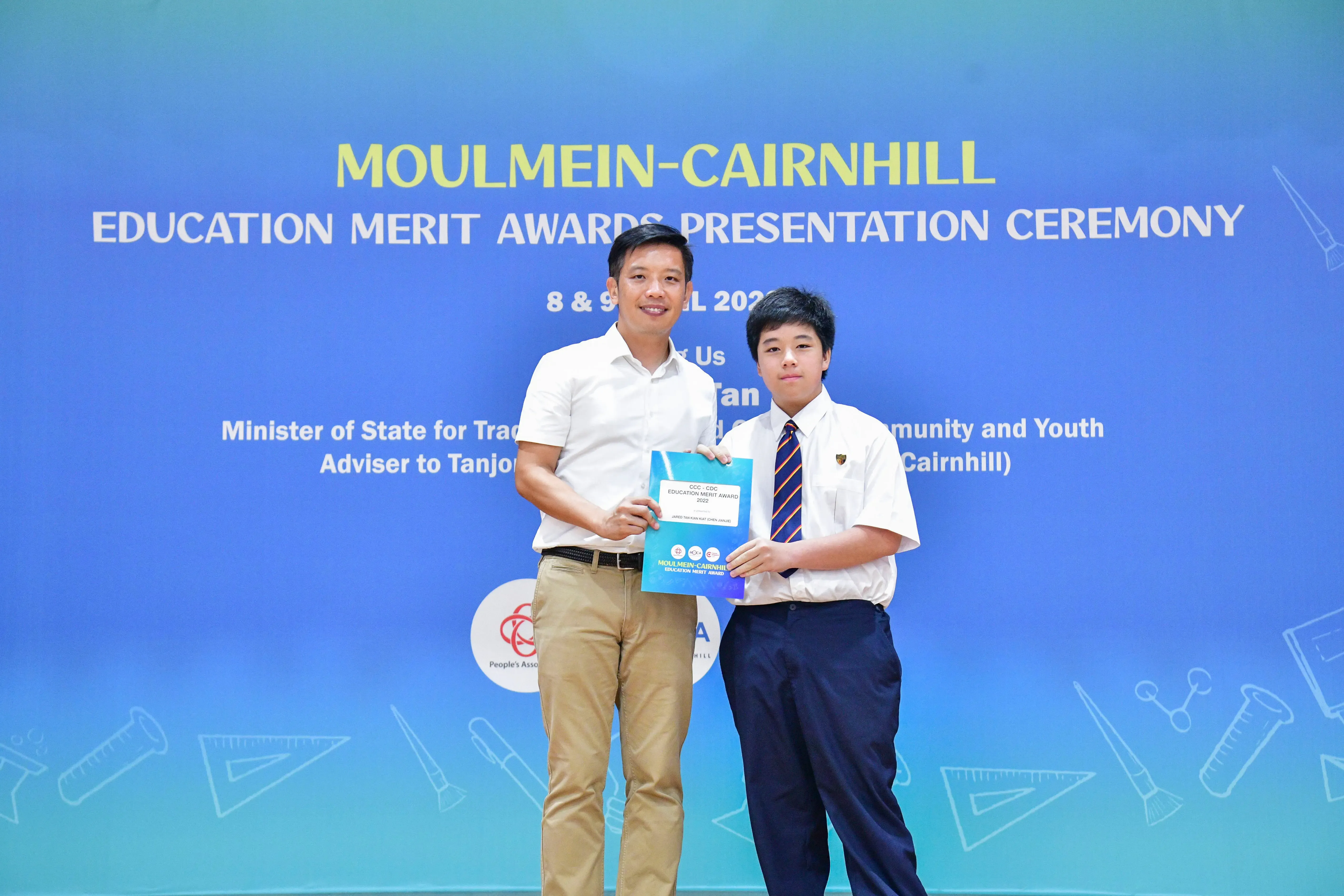 An adult and a uniformed student hold an award certificate at the Moulmein-Cairnhill Education Merit Awards Ceremony.