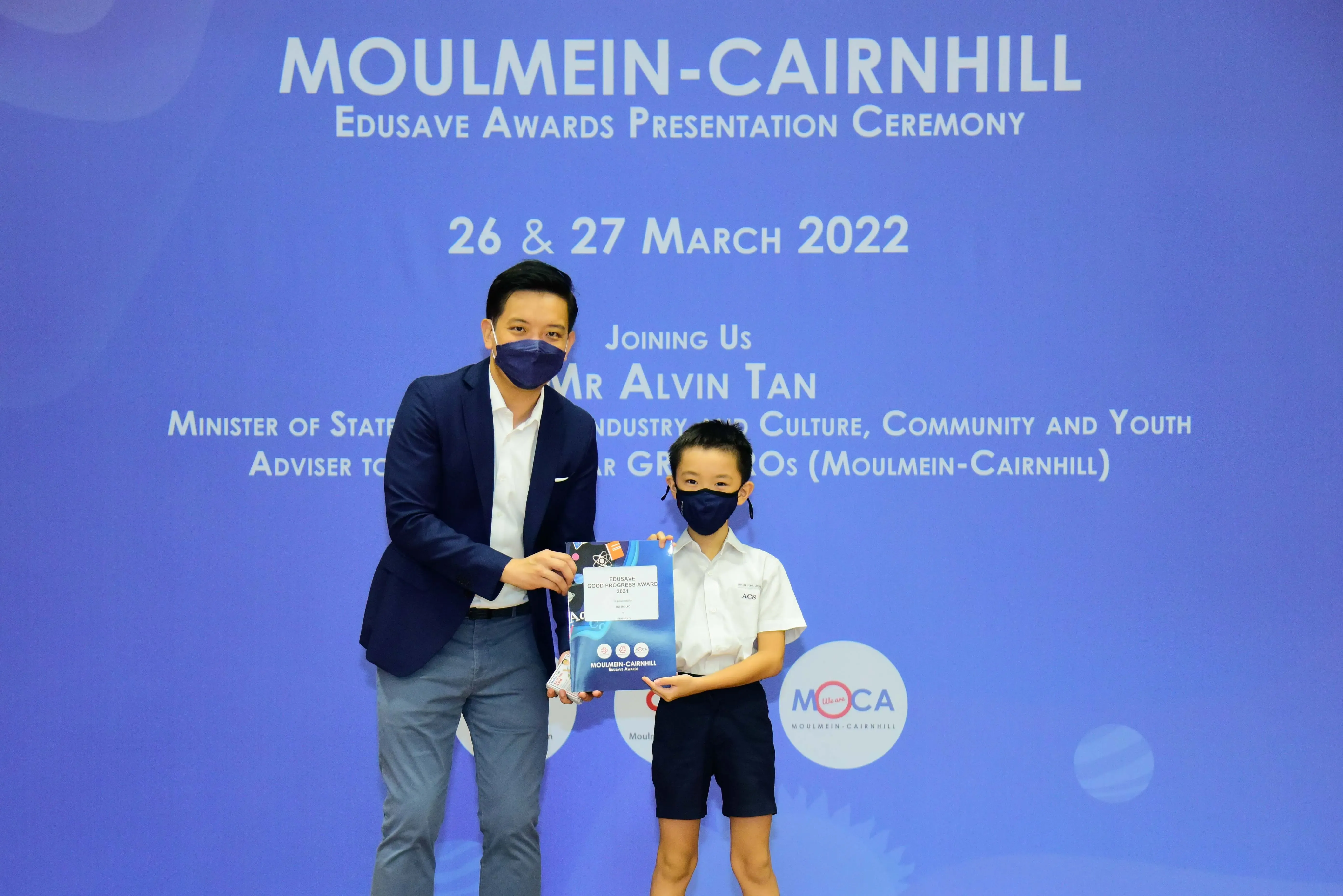 A man and a young student in school uniform hold an award at the Moulmein-Cairnhill Edusave Awards Ceremony, March 2022.