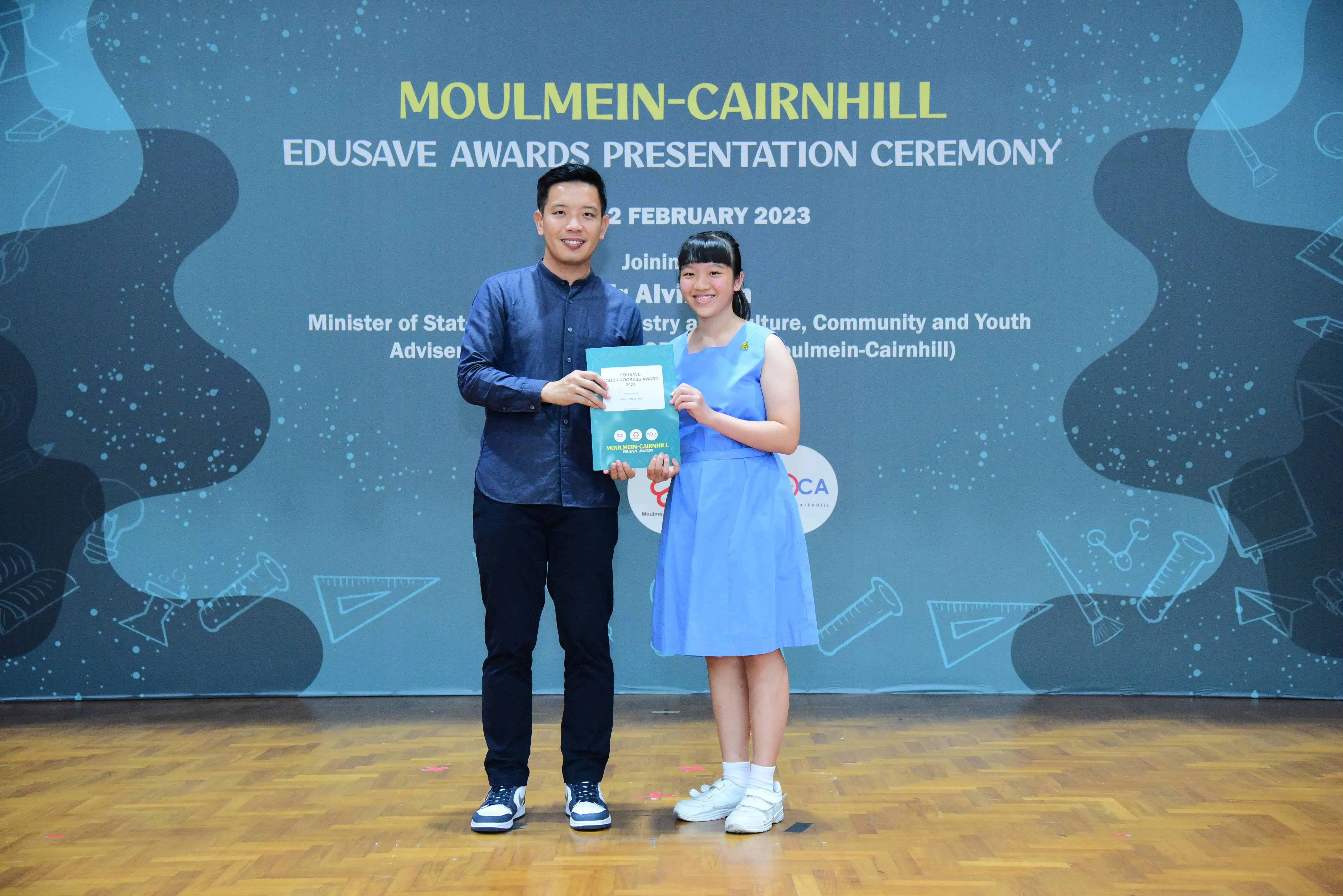 A man and a young girl hold a certificate together at the Moulmein-Cairnhill Edusave Awards Presentation Ceremony 2023.