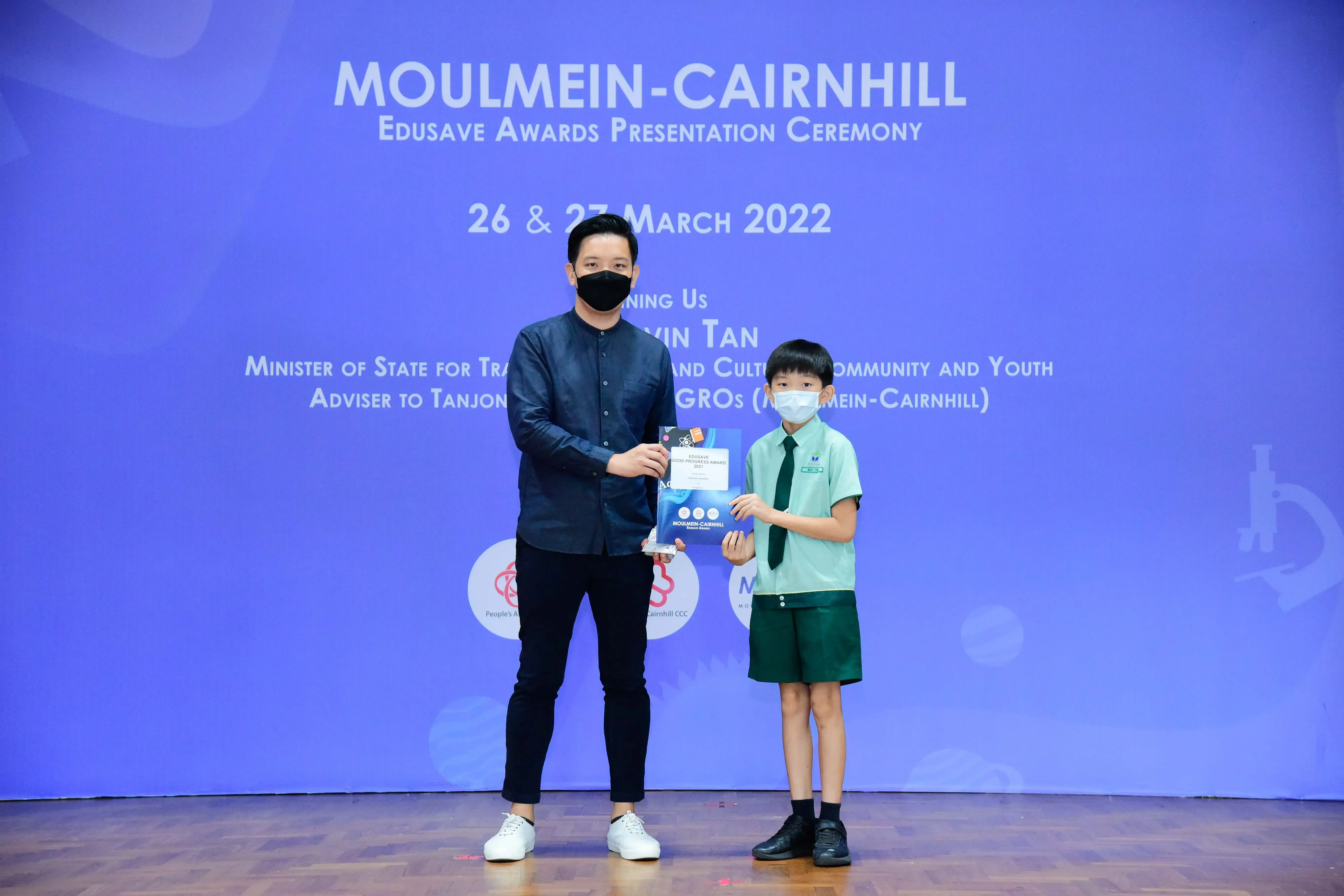 An adult and a young student in school uniform hold an award at the Moulmein-Cairnhill Edusave Awards Ceremony 2022.