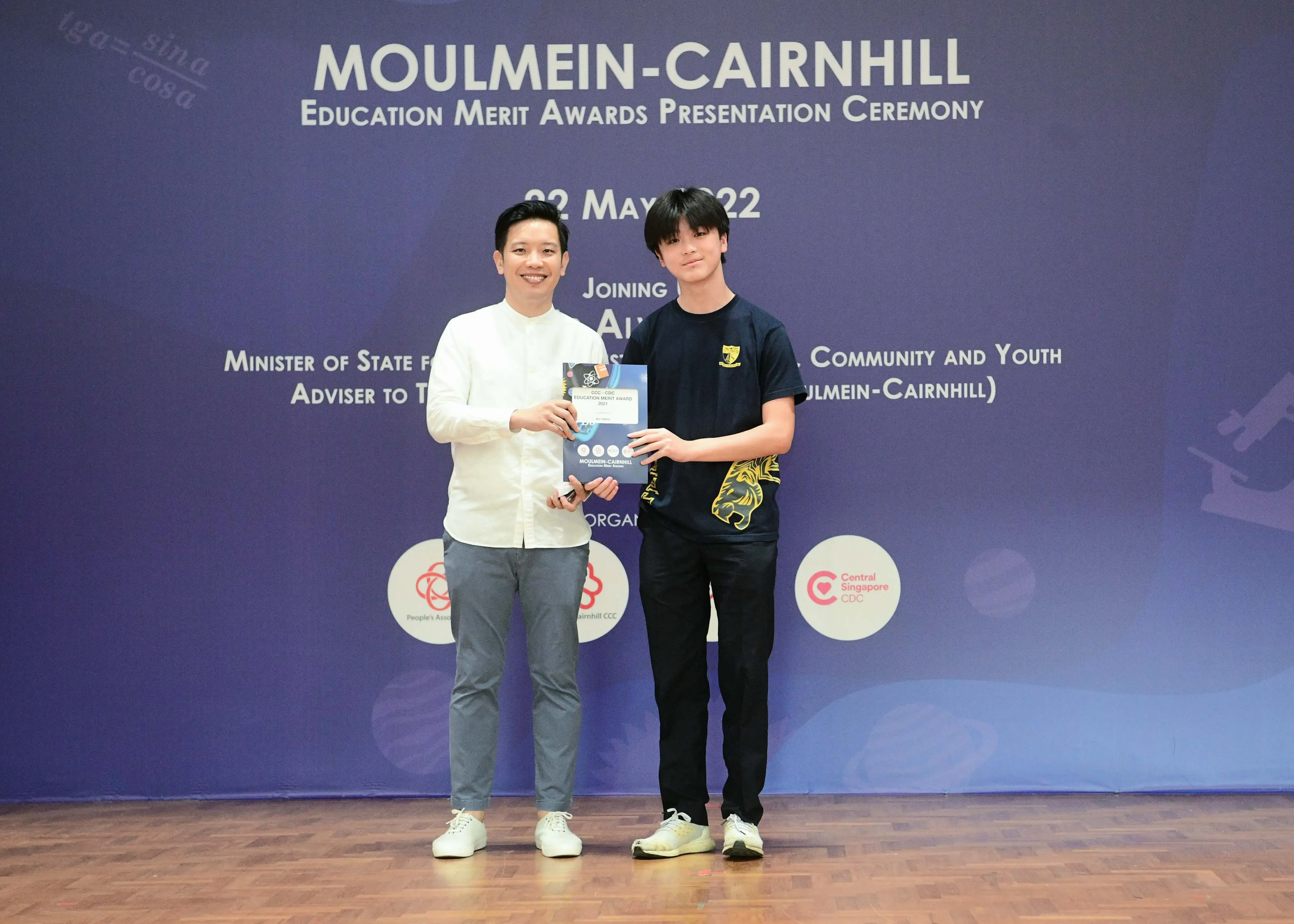 Two people hold a certificate at the Moulmein-Cairnhill Education Merit Awards Presentation Ceremony on 2 May 2022.