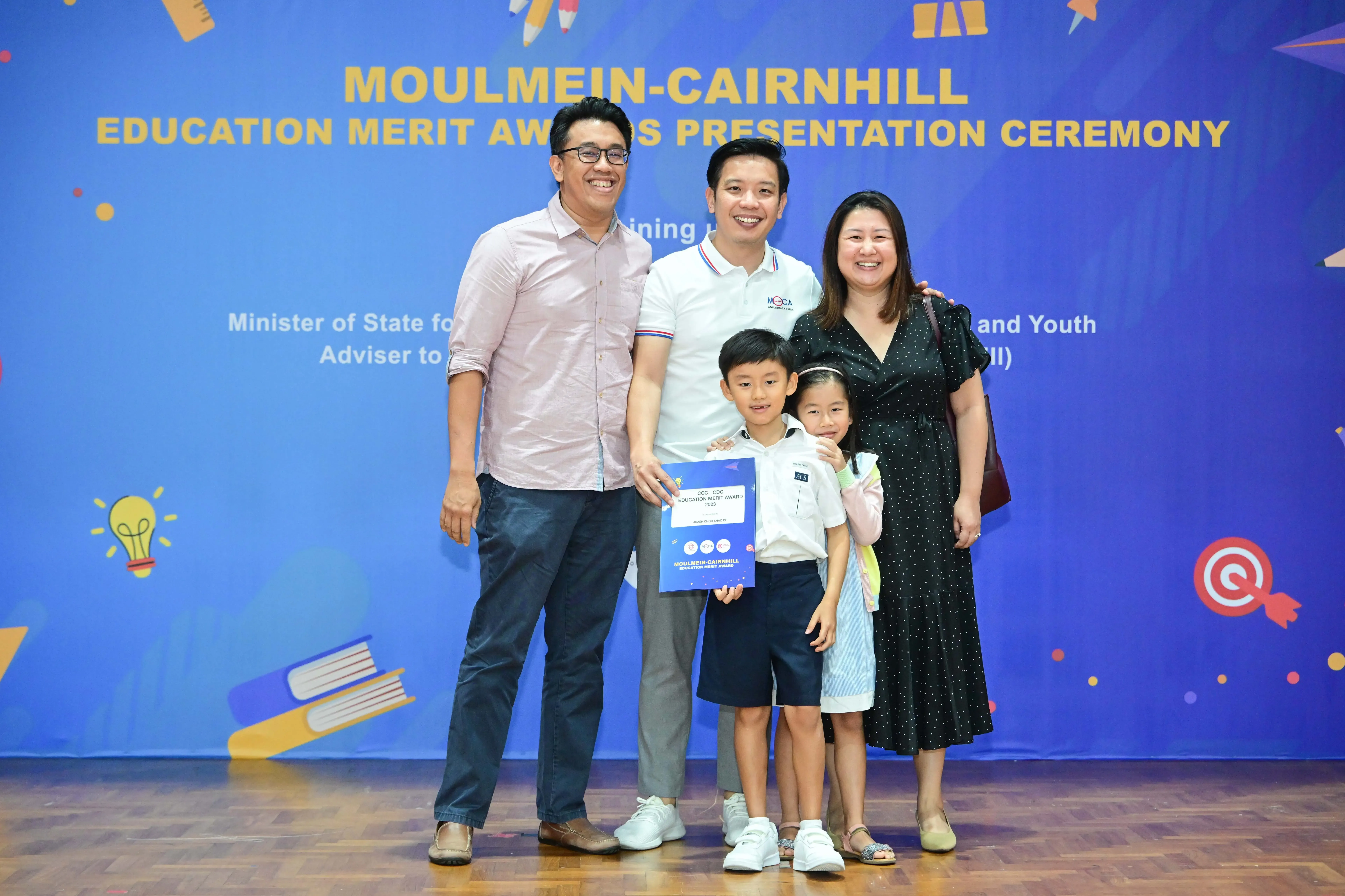 Three adults and two children pose with an award certificate at the Moulmein-Cairnhill Education Merit Awards ceremony.