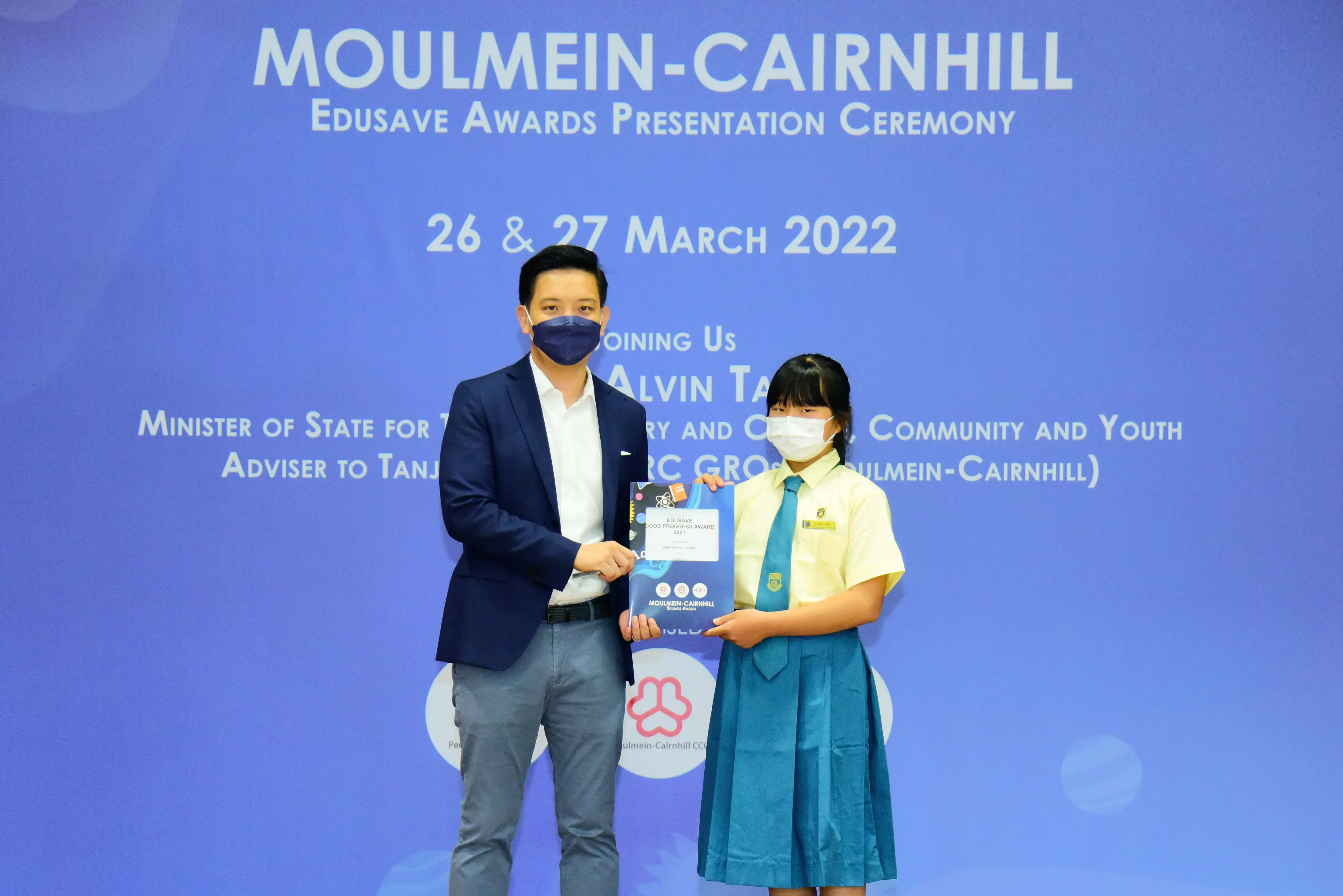 A man in a blazer presents an award to a uniformed schoolgirl at the Moulmein-Cairnhill Edusave Awards Ceremony 2022.