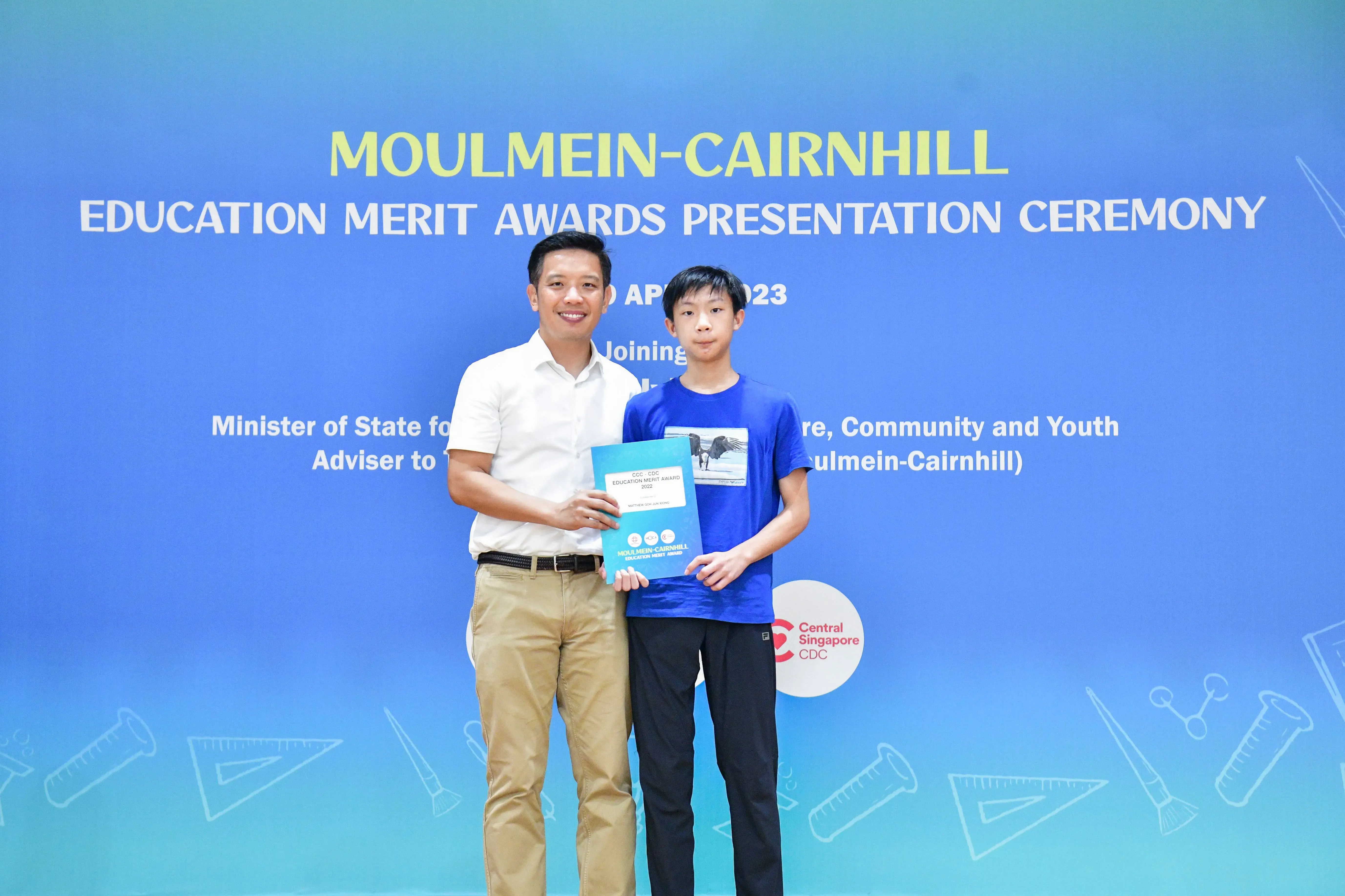A man and a boy pose holding an award folder at the Moulmein-Cairnhill Education Merit Awards Ceremony 2023.