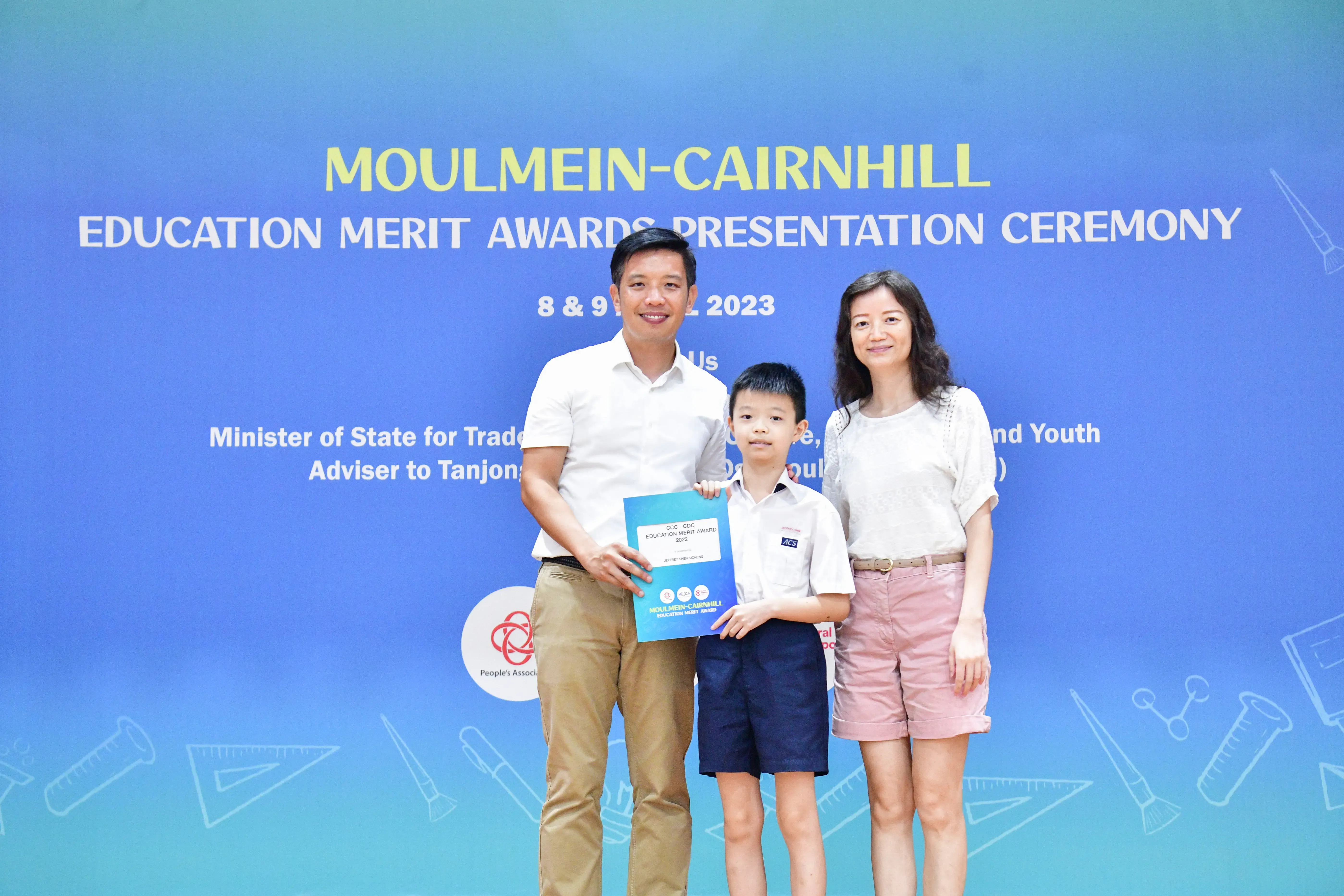 A boy holding an award certificate stands between two adults at the Moulmein-Cairnhill Education Merit Awards 2023.