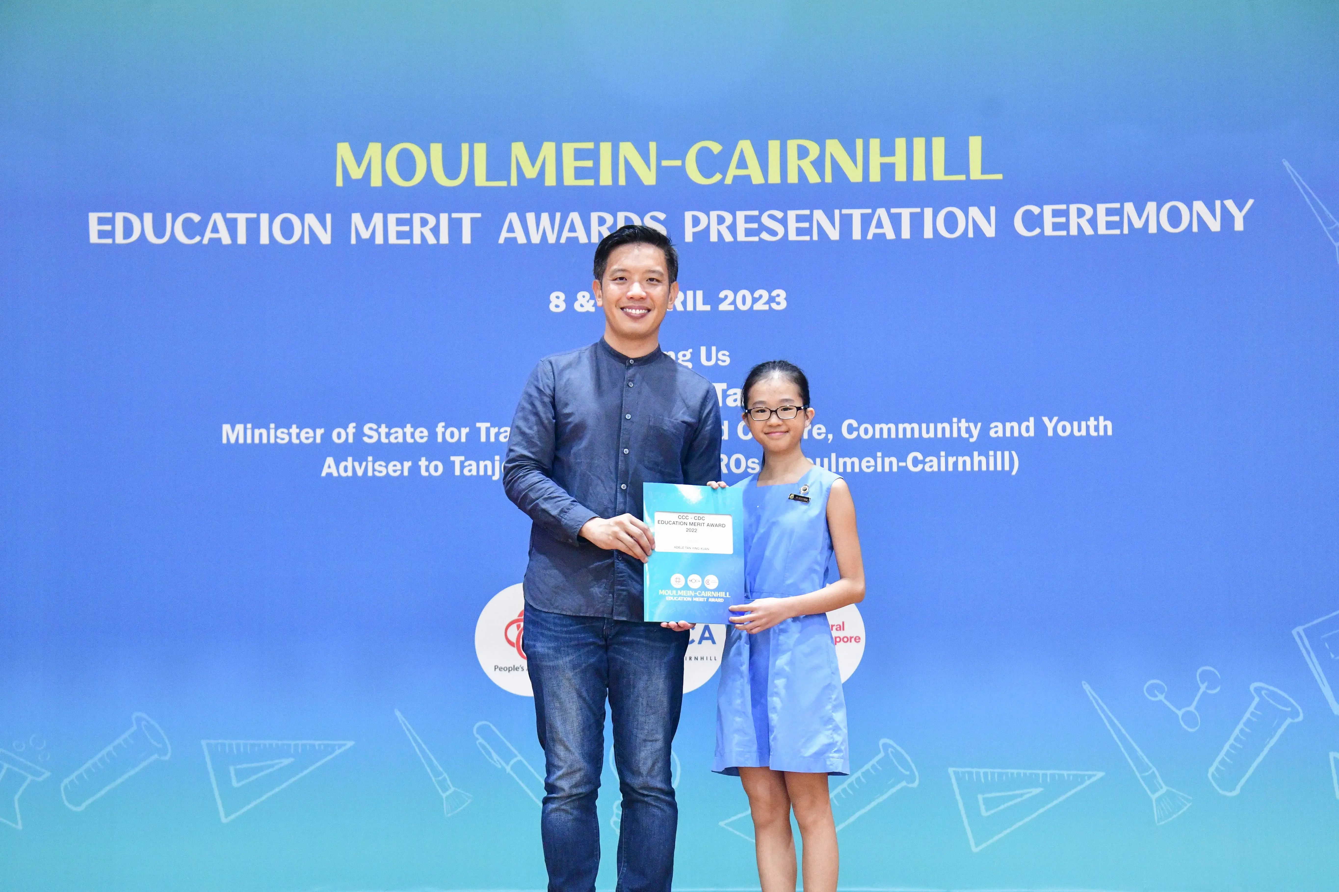 A man and a young girl hold a certificate together at the Moulmein-Cairnhill Education Merit Awards Ceremony 2023.