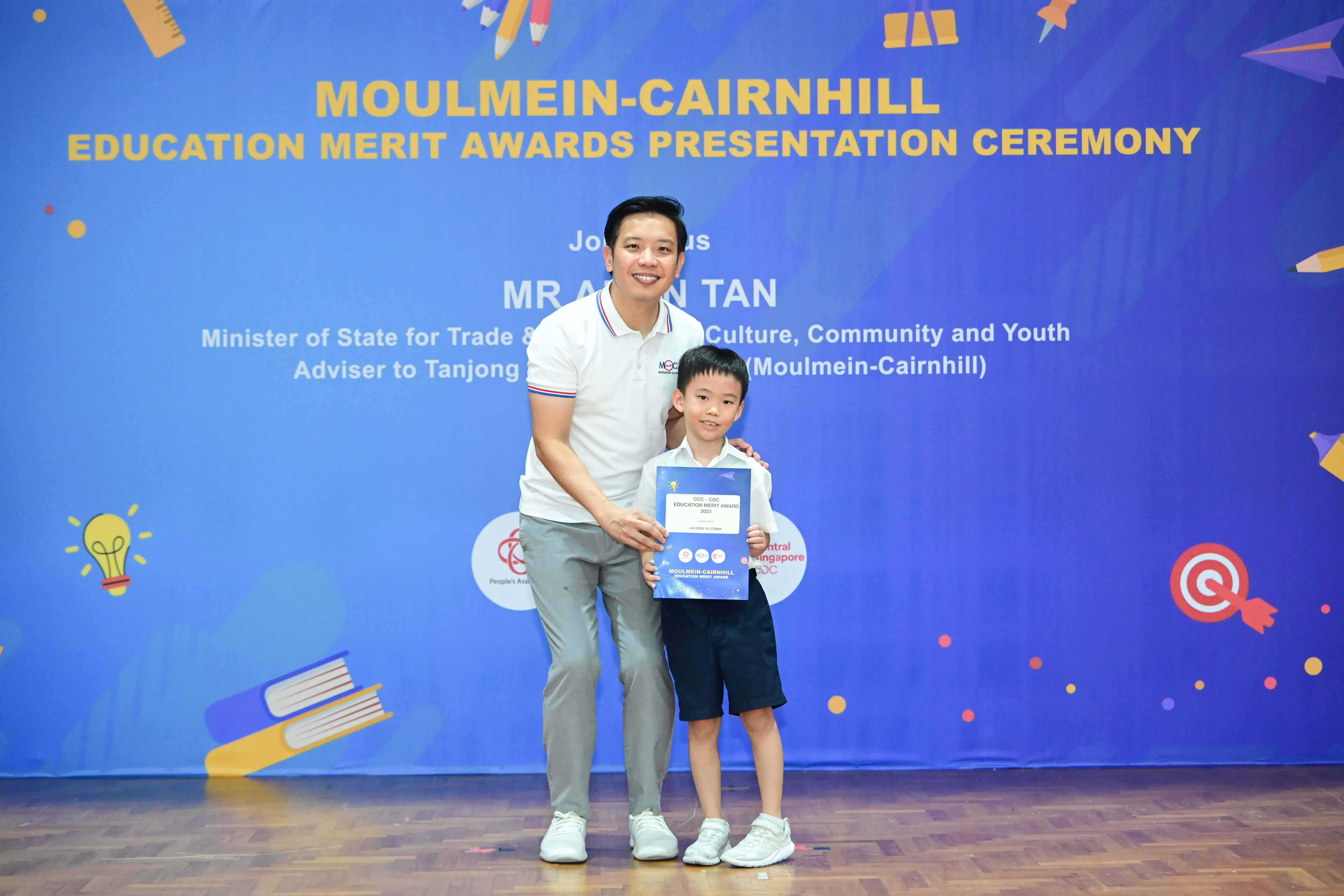 A man and young boy pose holding an award certificate at the Moulmein-Cairnhill Education Merit Awards ceremony.
