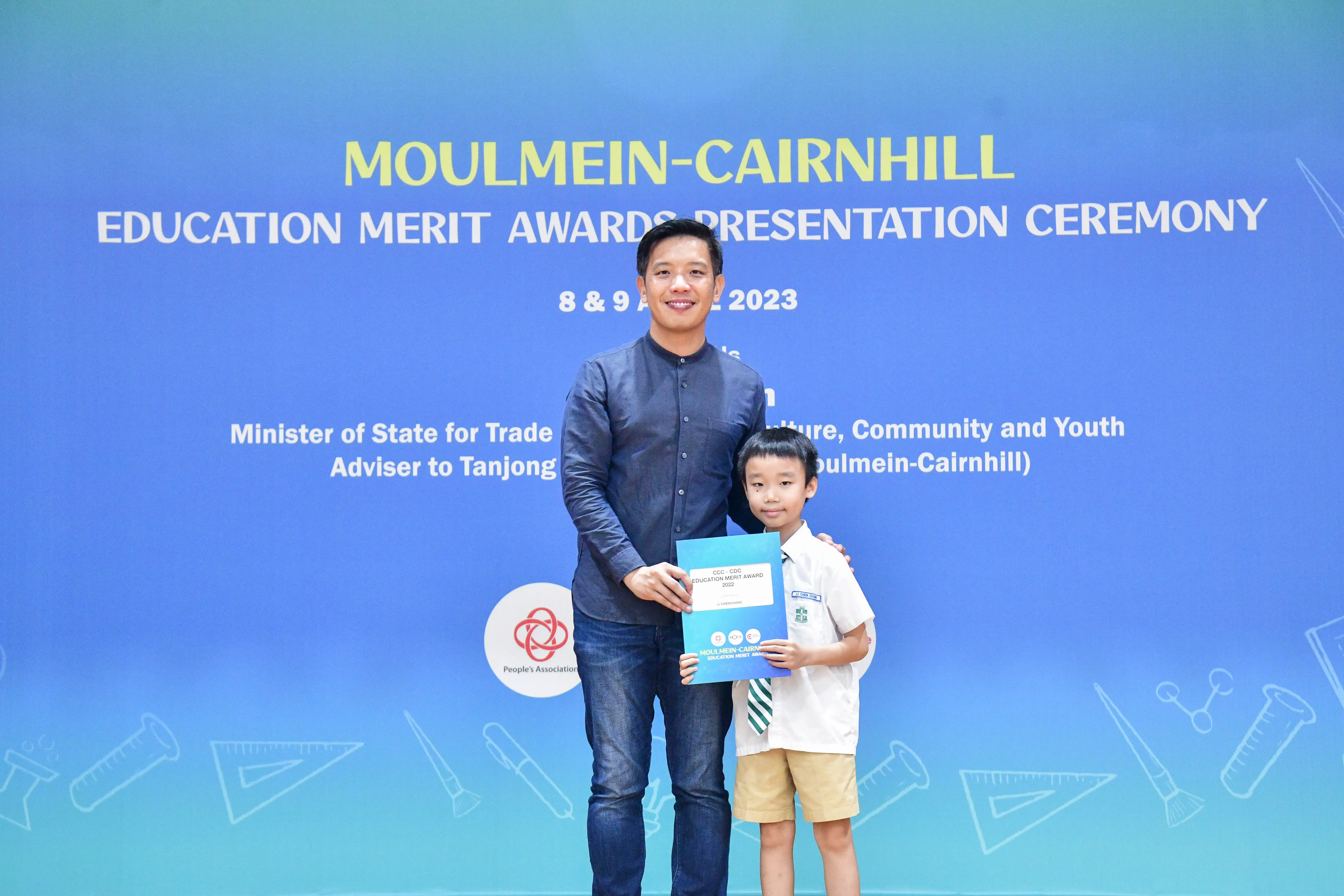 Man and young boy hold a certificate together at the Moulmein-Cairnhill Education Merit Awards Ceremony 2023.