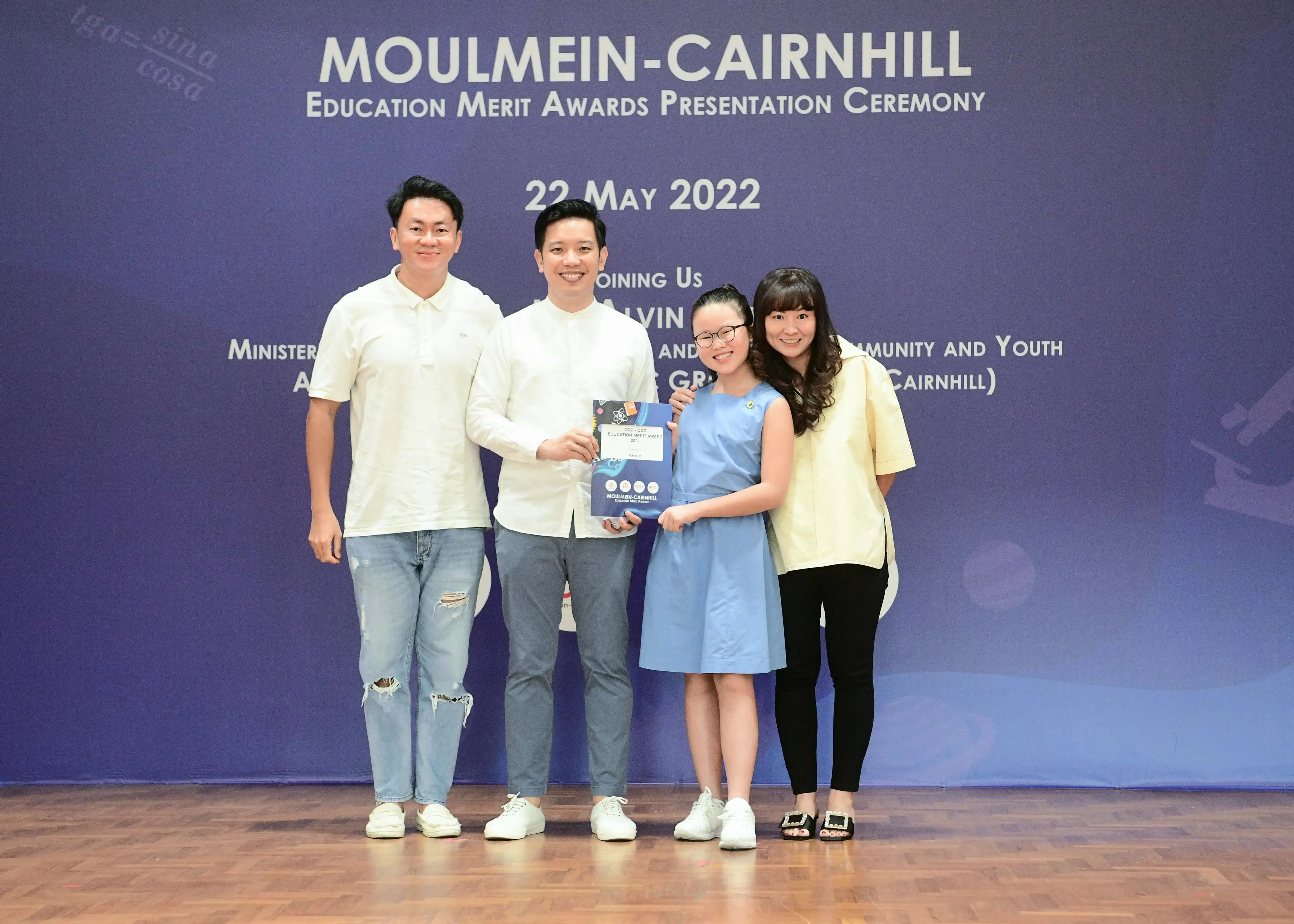 Four people smile on a stage at the Moulmein-Cairnhill Education Merit Awards Ceremony on 22 May 2022.