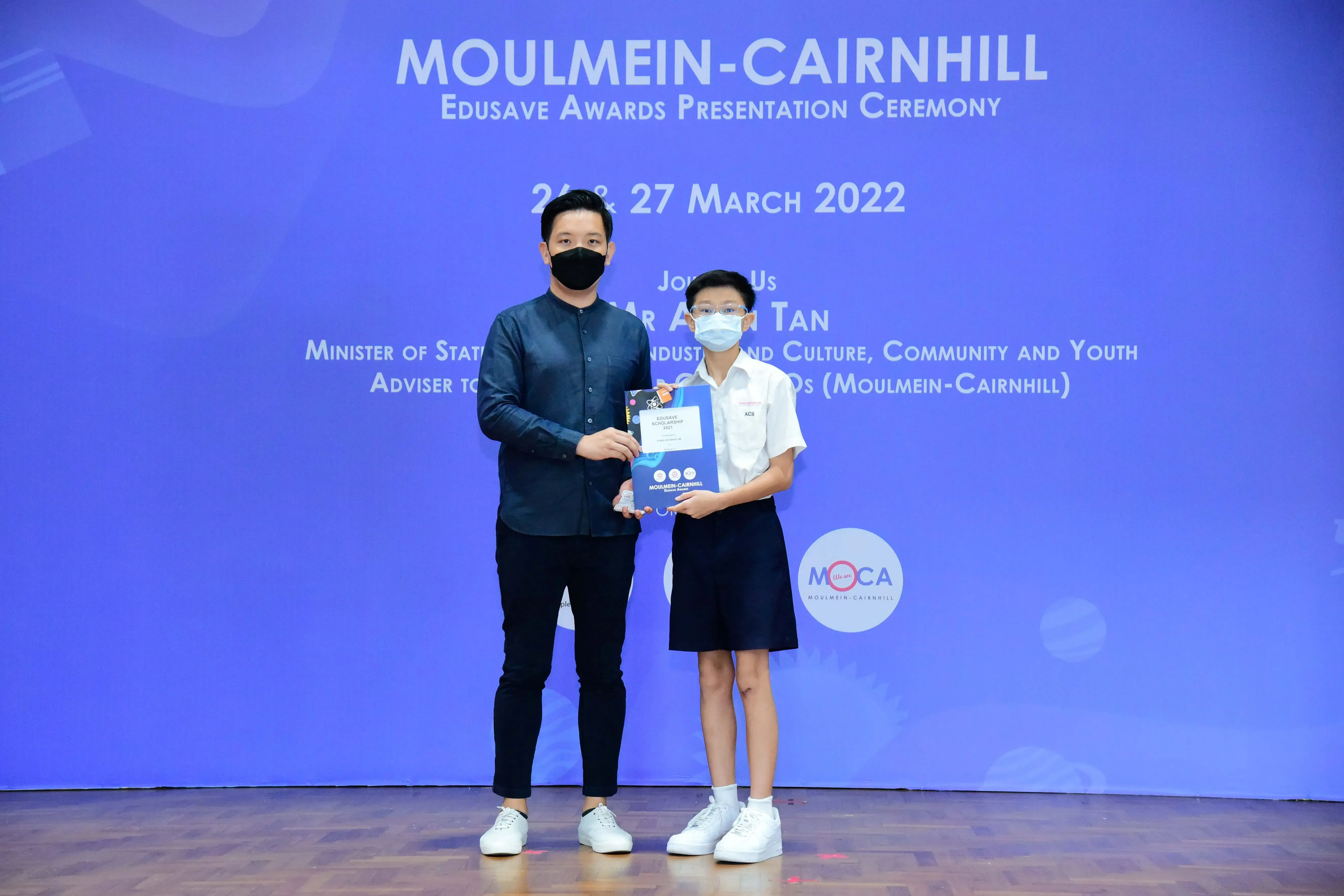 An adult and a child wearing masks hold a certificate at the Moulmein-Cairnhill Edusave Awards Ceremony, March 2022.